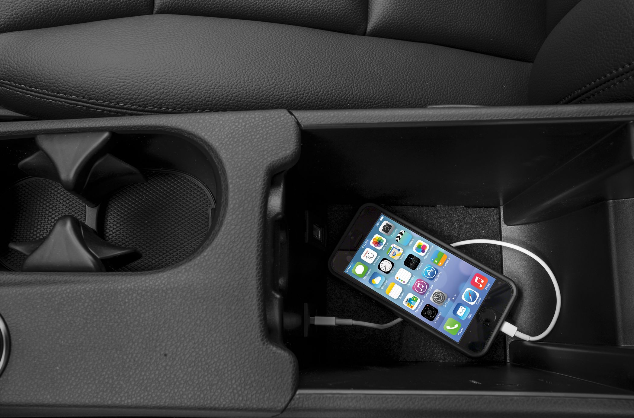 Center console with charging port, cup holders, and smartphone connected.