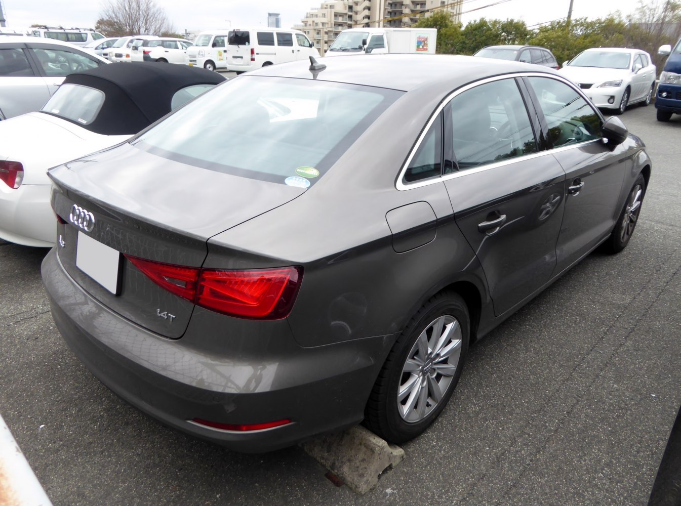 Rear-side view of a grey sedan with tail lights and alloy wheels.