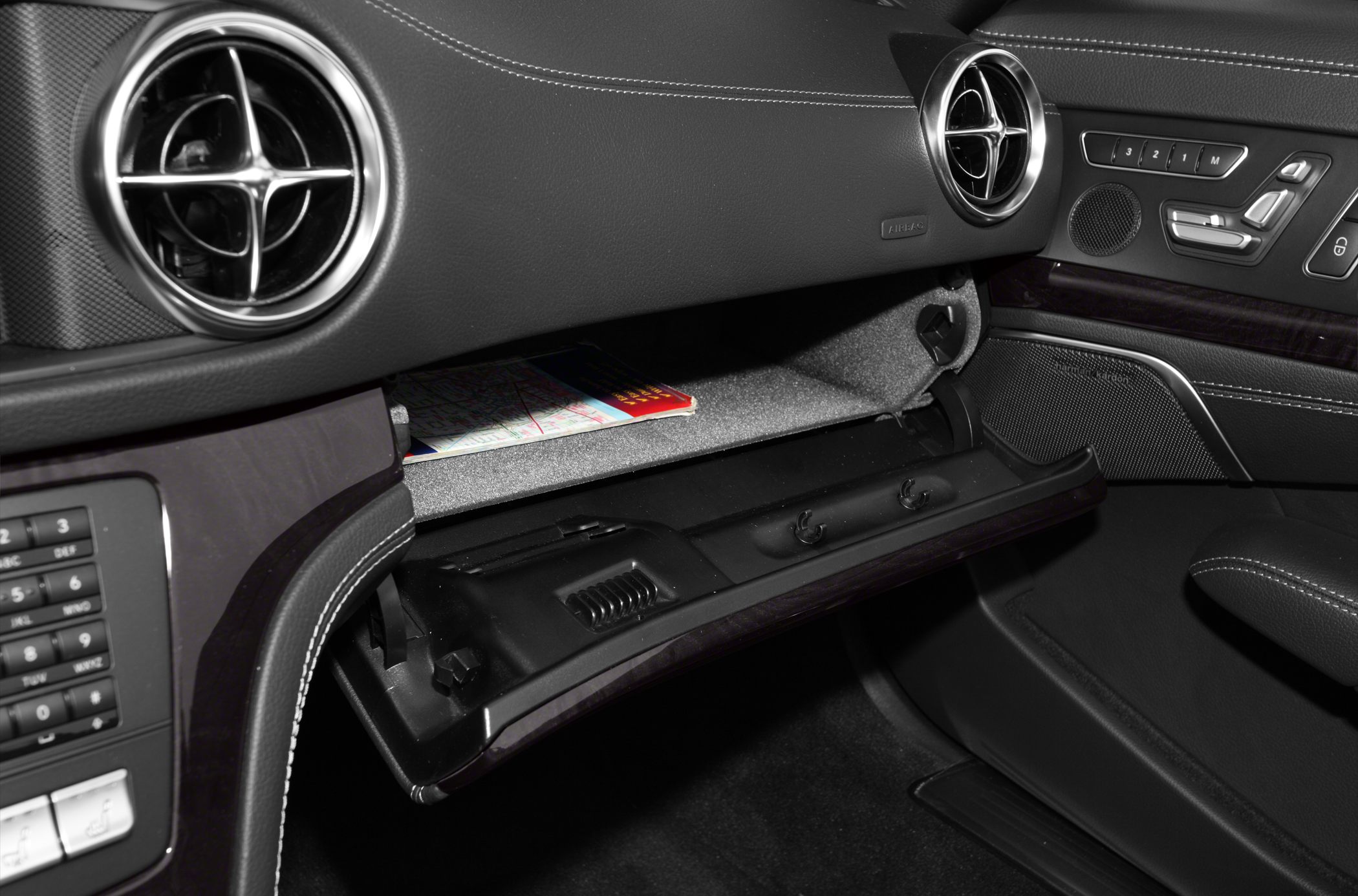 Open glove compartment, circular air vents, and seat adjustment controls in a luxury car interior