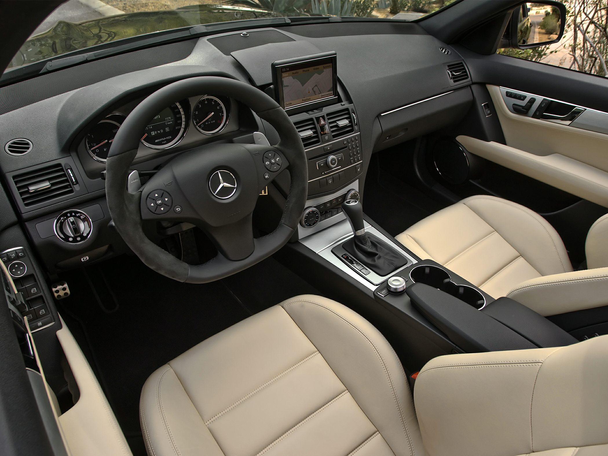 Luxury sedan interior with steering wheel, navigation screen, and beige leather seats.