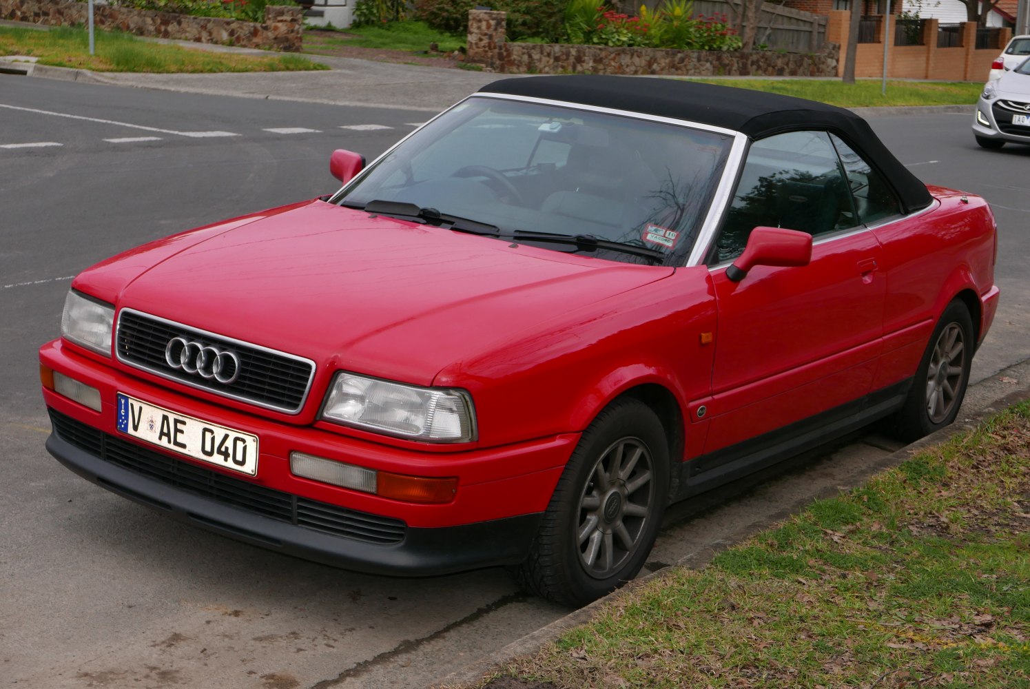 Red convertible with black soft top and alloy wheels parked on street.