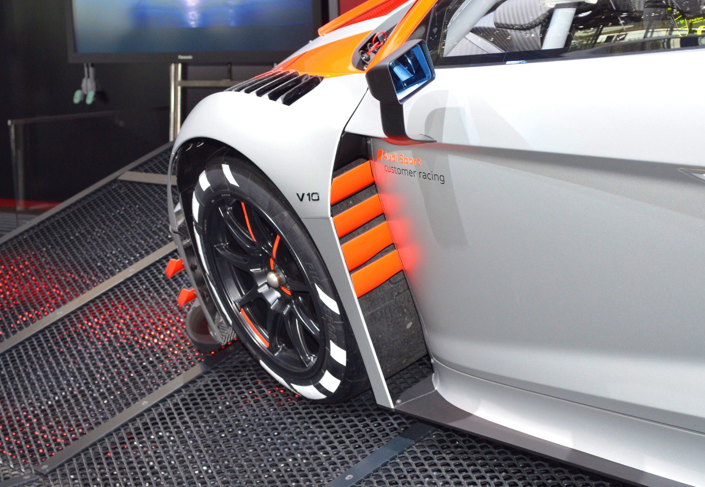 Close-up of racing wheel, V10 badge, and orange side vent with Audi Sport decal