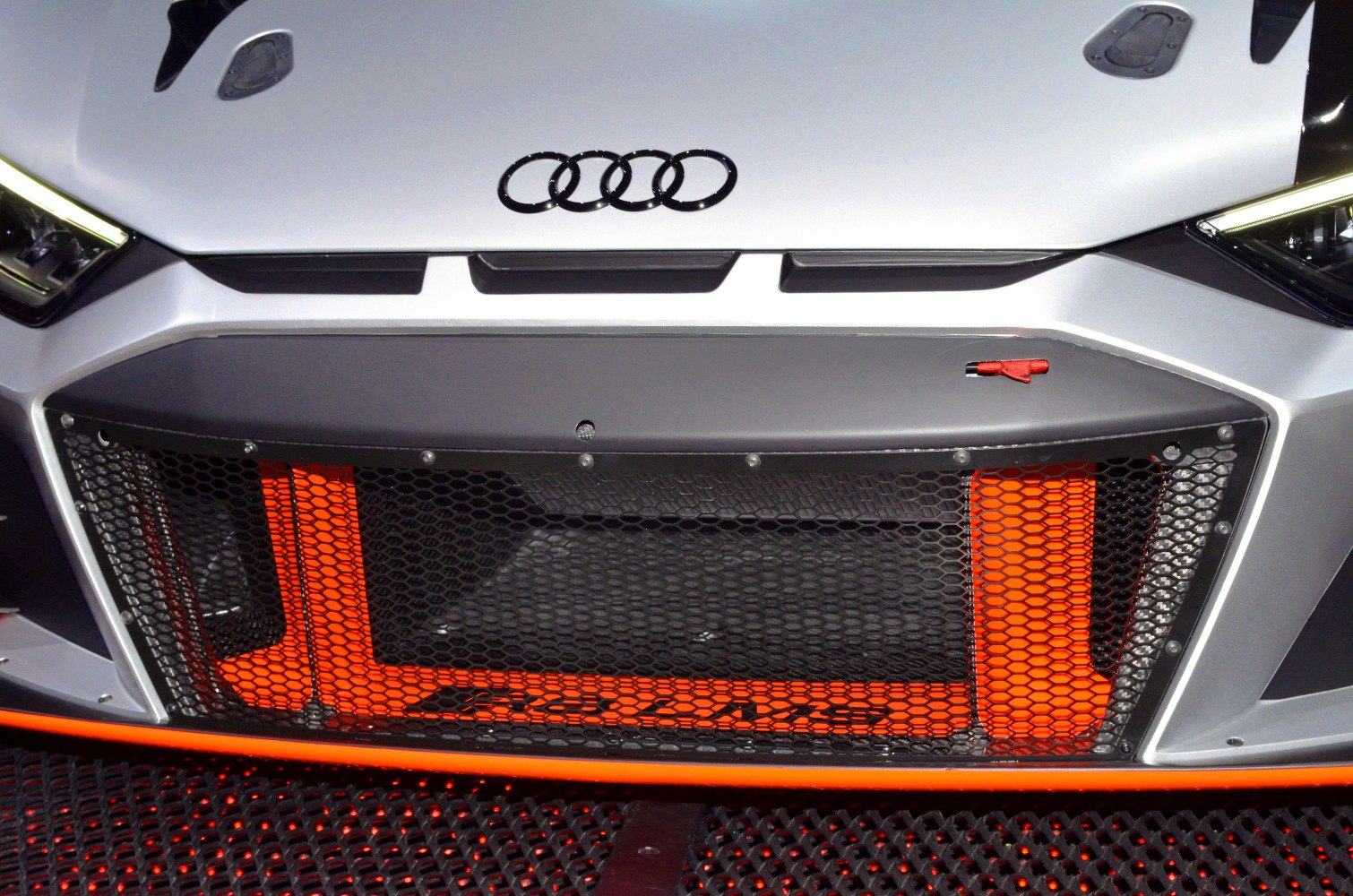 Front grille mesh with orange accents and Audi rings.