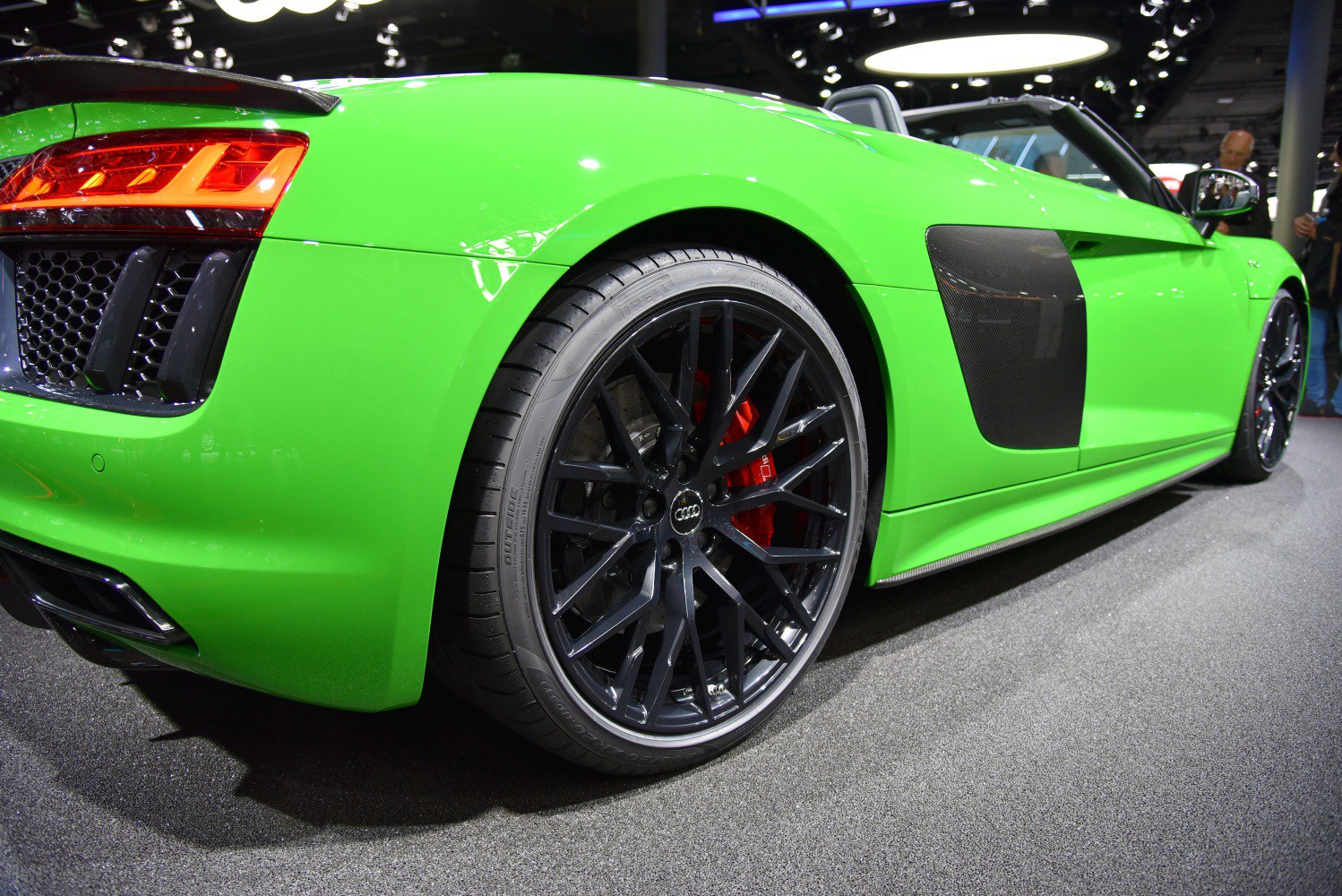 Close-up of black rear alloy wheel and side air intake on green convertible.