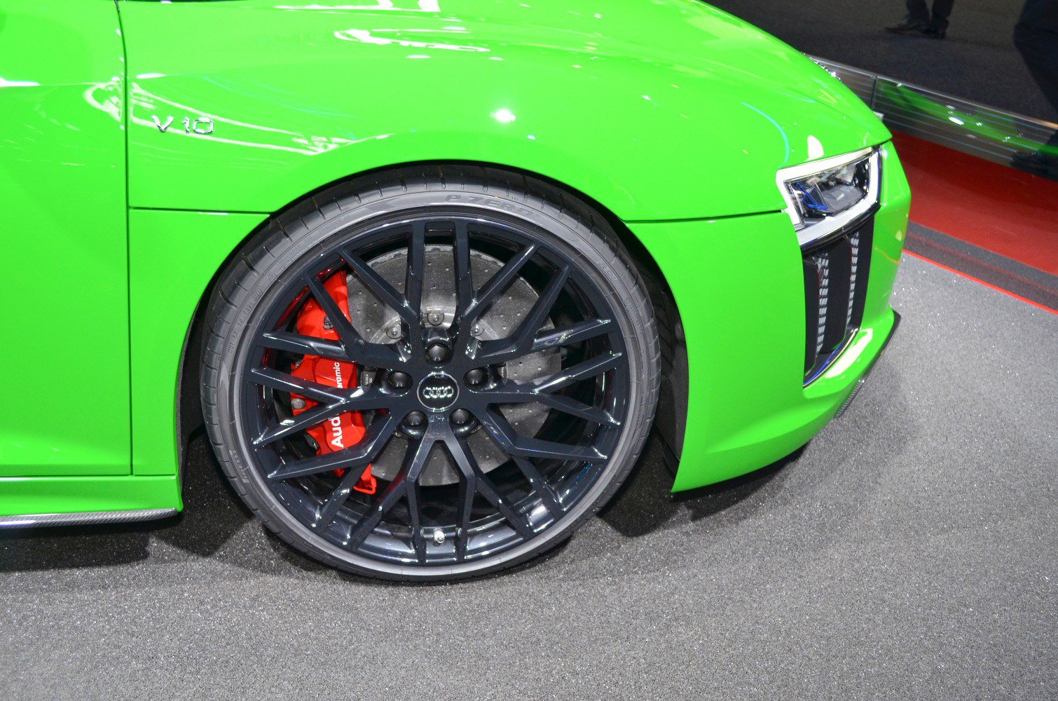 Close-up of front wheel with black alloy rims and red brake calipers, plus LED headlight.