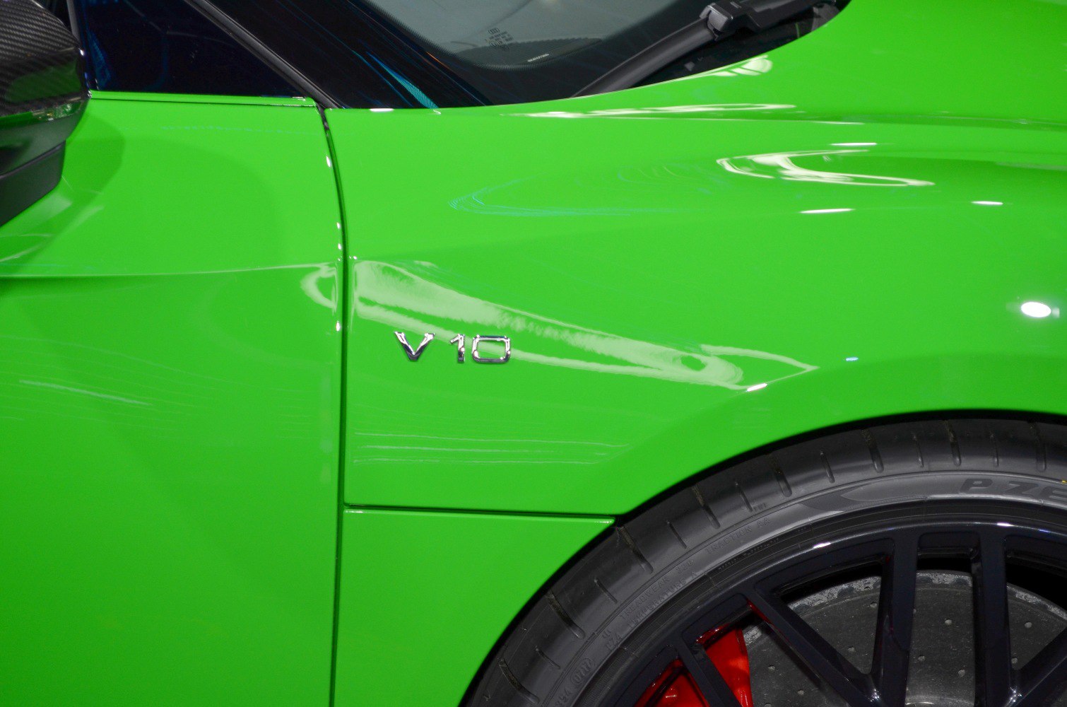 V10 badge and rear wheel with red brake caliper on green sports car.