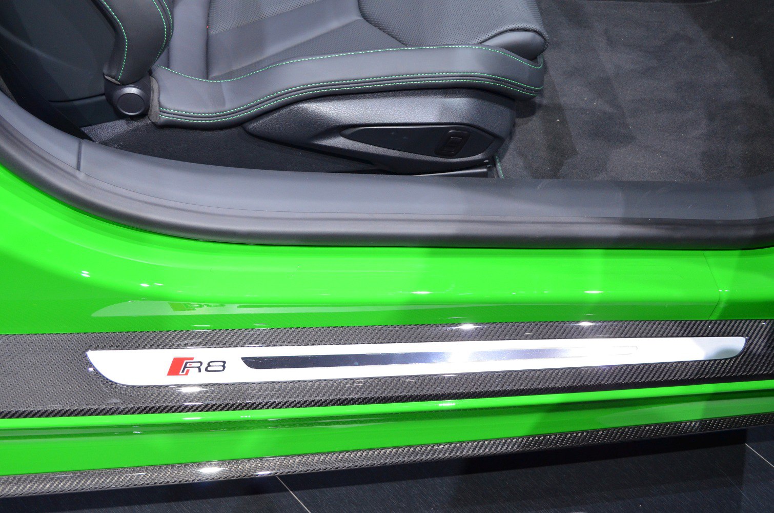 Close-up of door sill with carbon fiber trim and seat base with green stitching