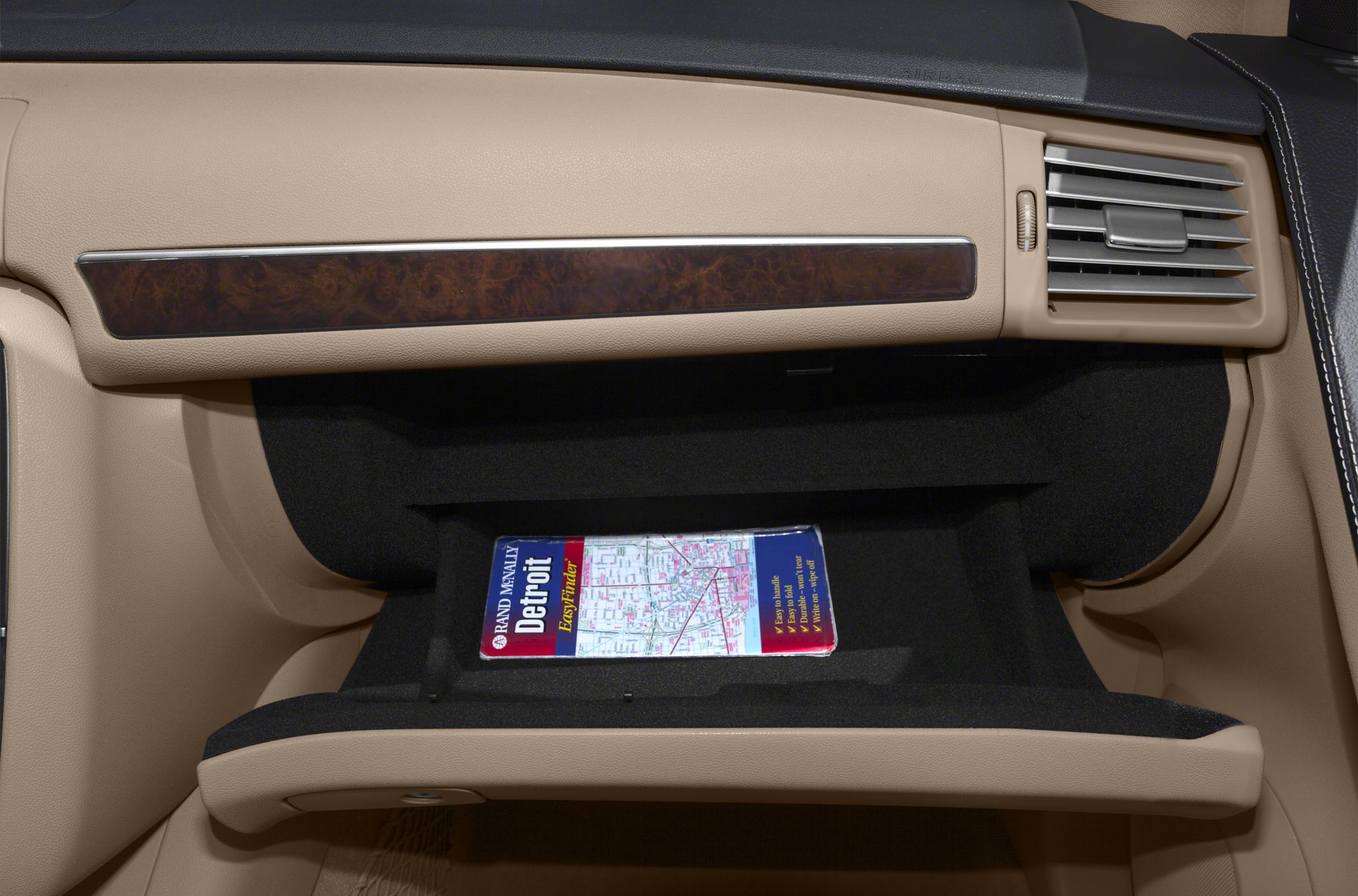 Open glove compartment with map, wood trim, beige interior, and air vent