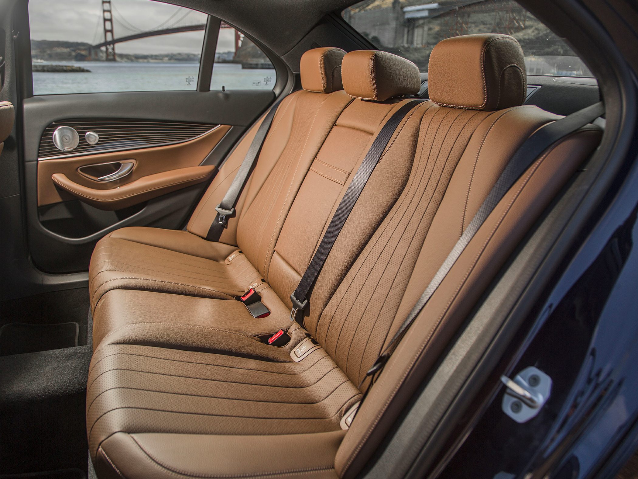 Tan leather rear seats with seat belts and detailed door panel in sedan interior