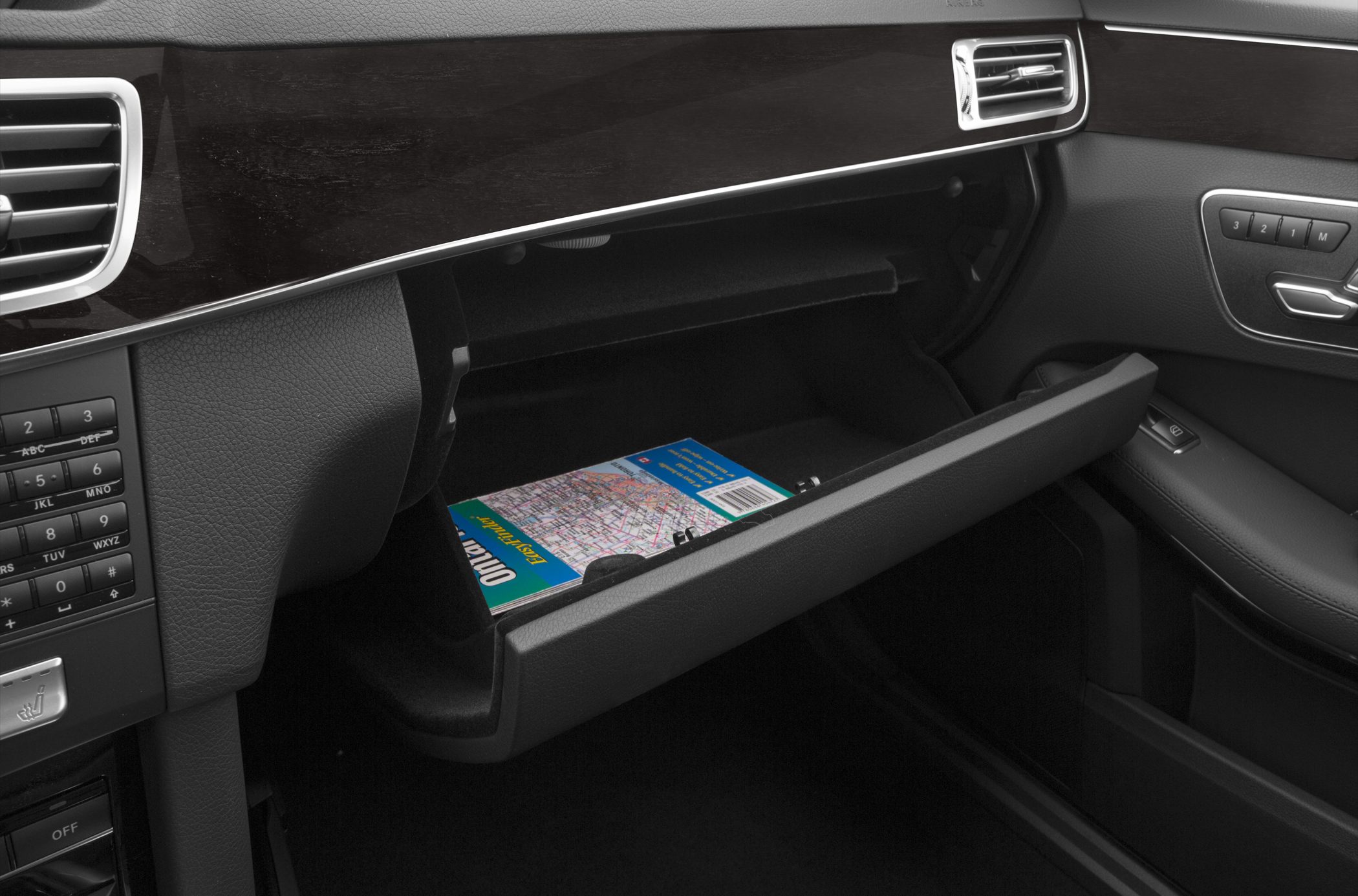 Open glovebox storage inside a car interior with control panel and door buttons
