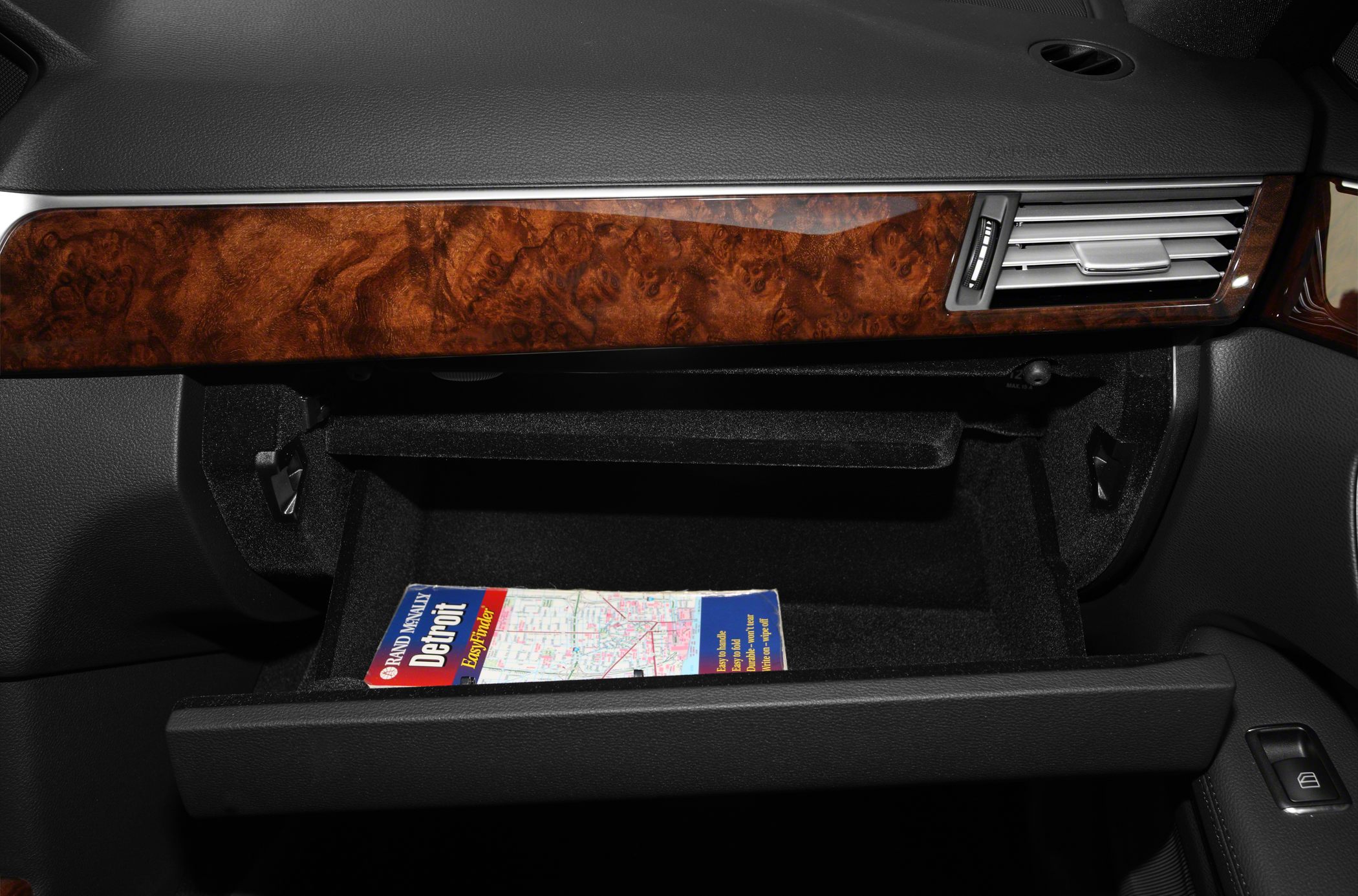 Open glove box with wood trim and air vent on dashboard