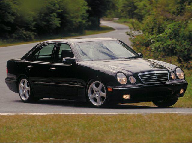 Black sedan with quad round headlights and five-spoke alloy wheels on road.
