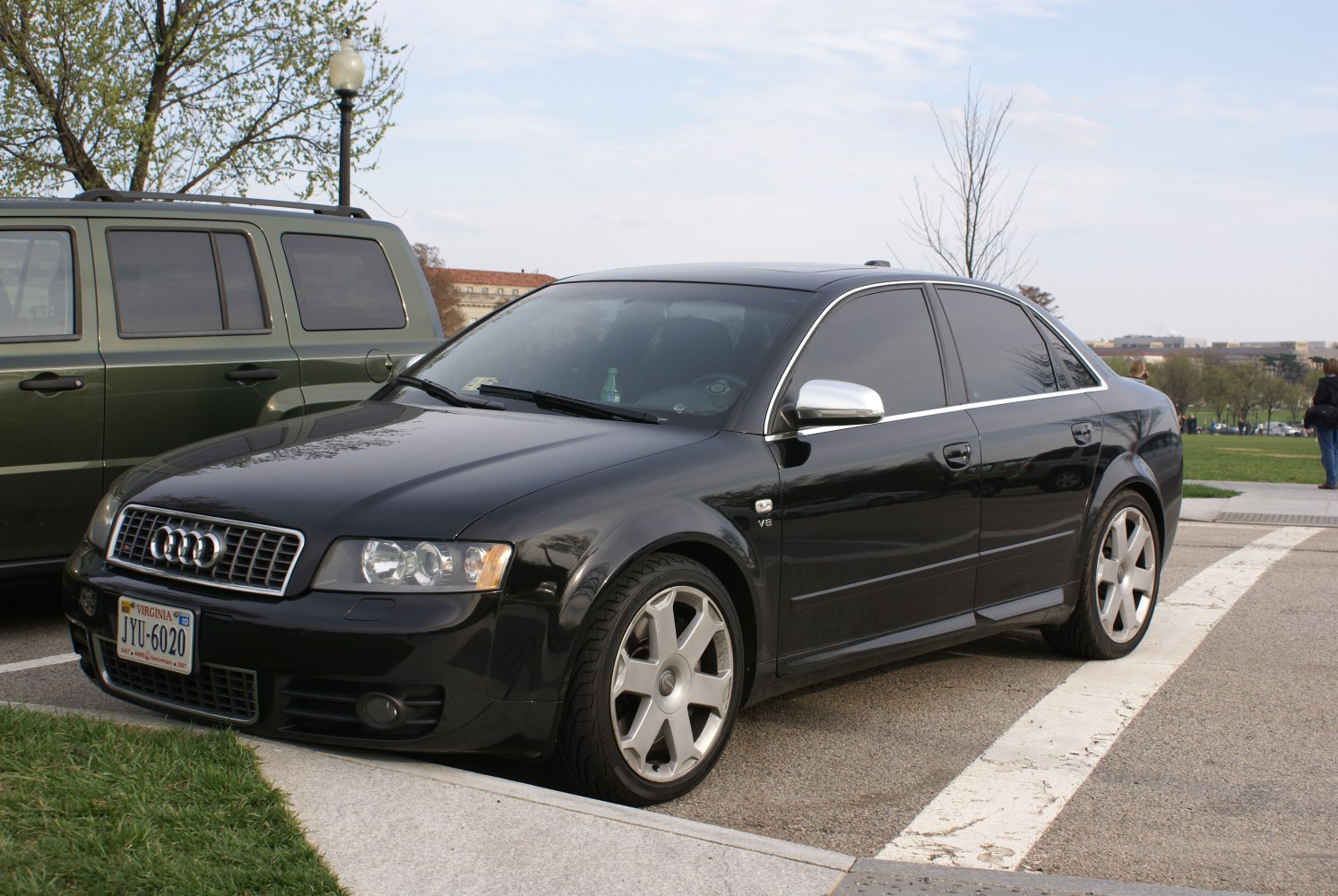 Black sedan with chrome mirrors, V8 badge, tinted windows, alloy wheels.