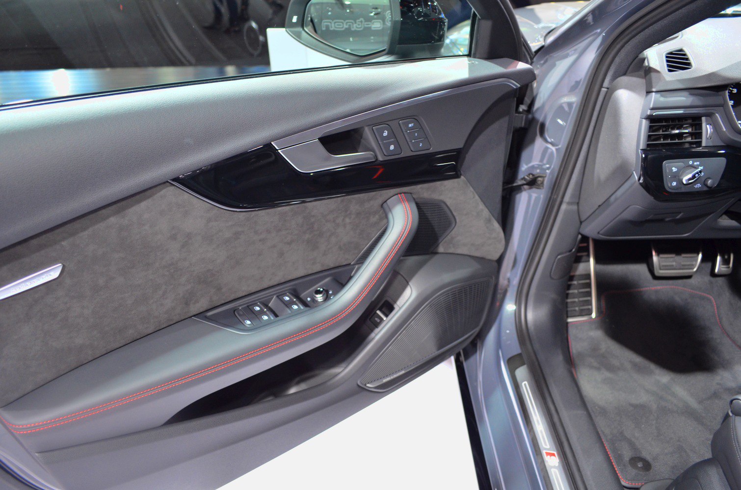 Interior driver door panel with control buttons and red contrast stitching