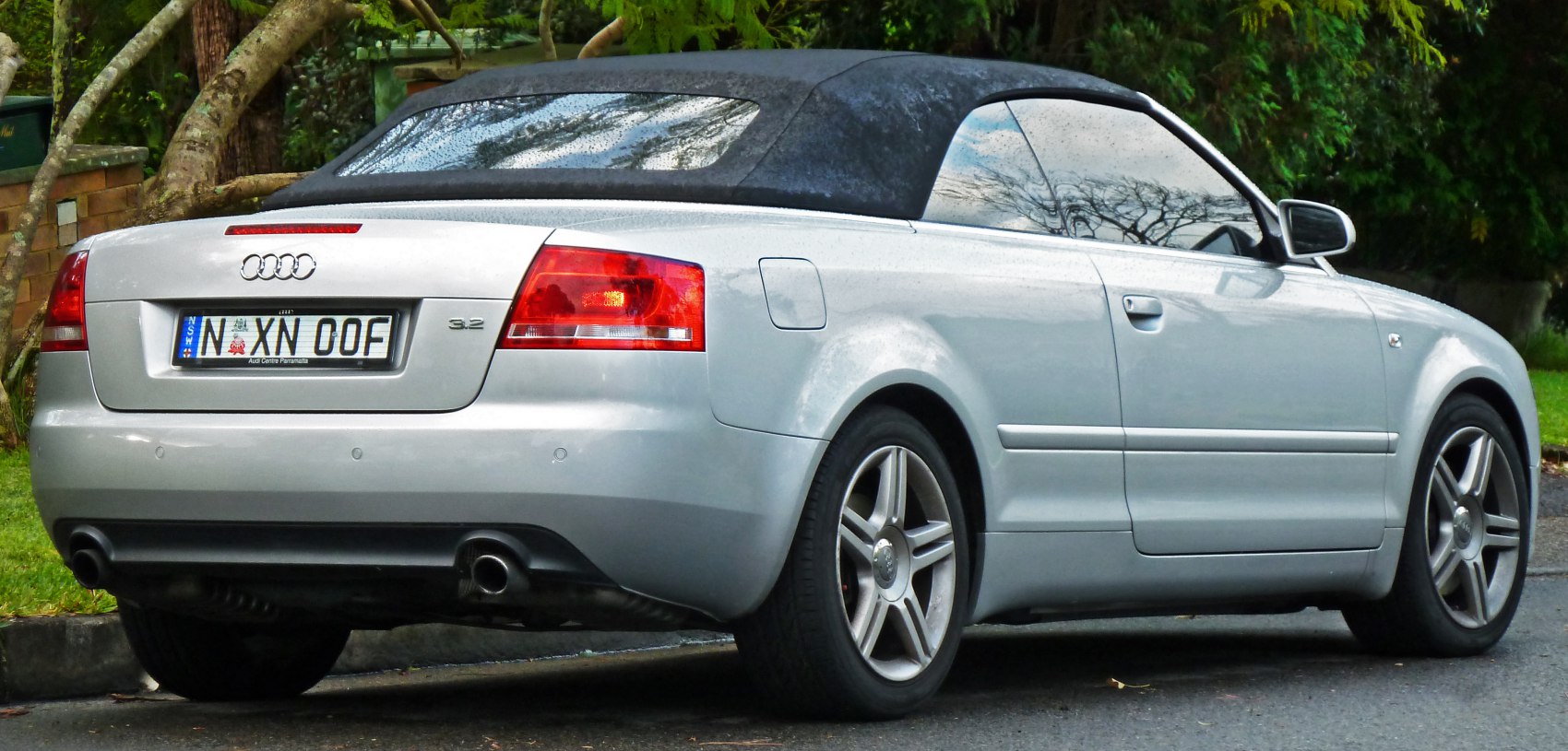 Silver convertible with soft top, rear-side view, alloy wheels, dual exhaust