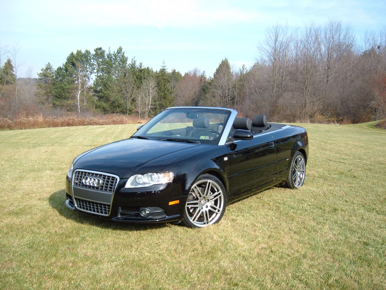Black convertible car with open top and alloy wheels in a grassy field