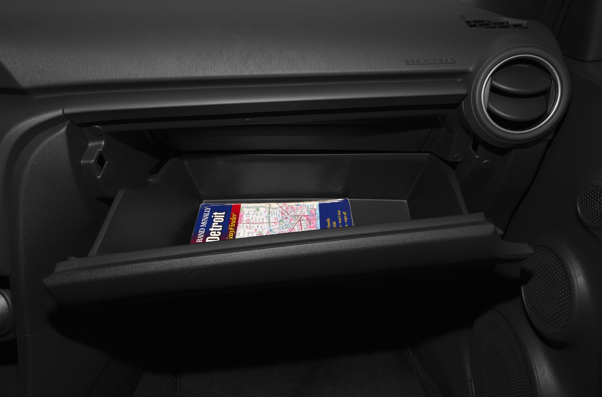 Open glove compartment with a map and circular air vent in car interior