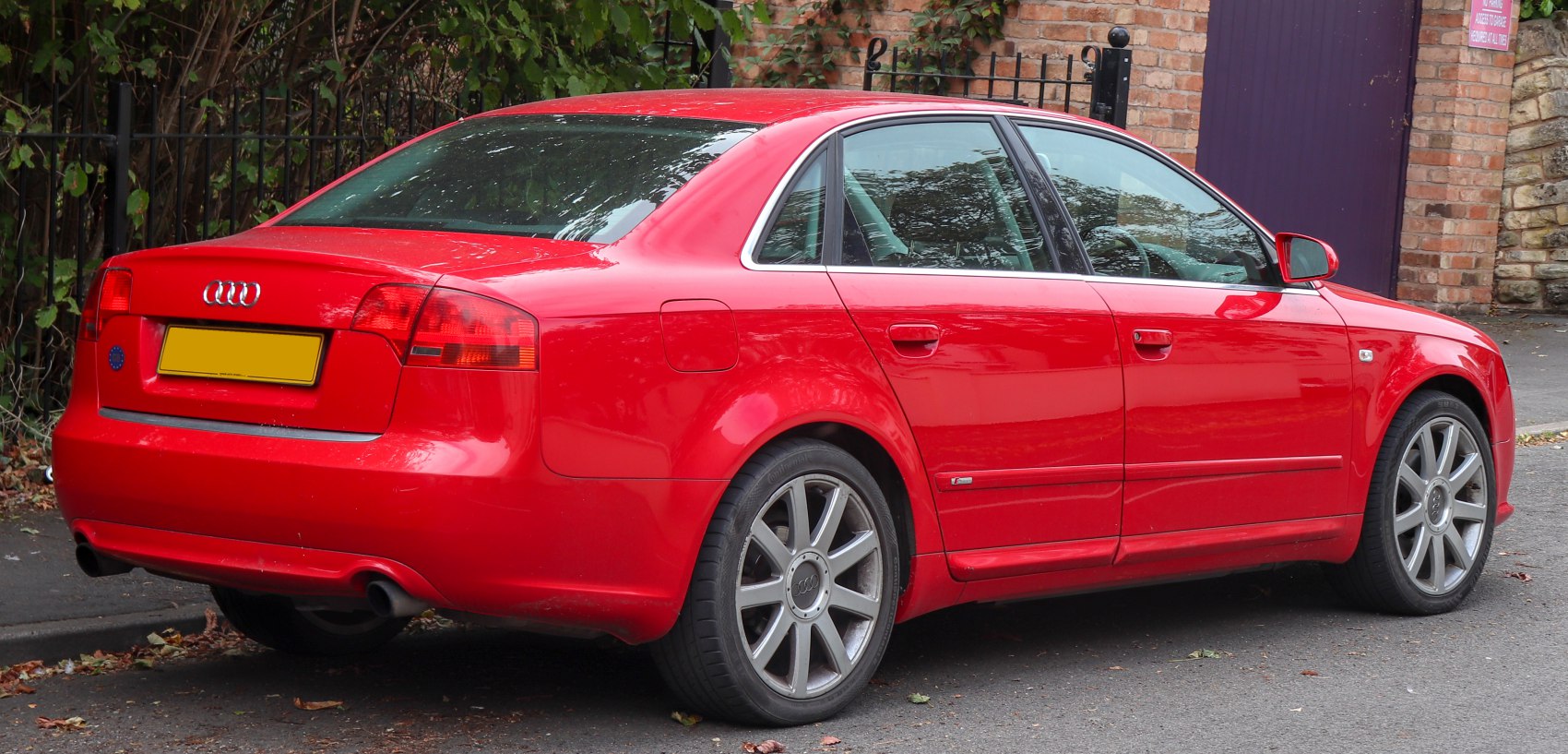 Red sedan rear-side view with alloy wheels and dual exhaust