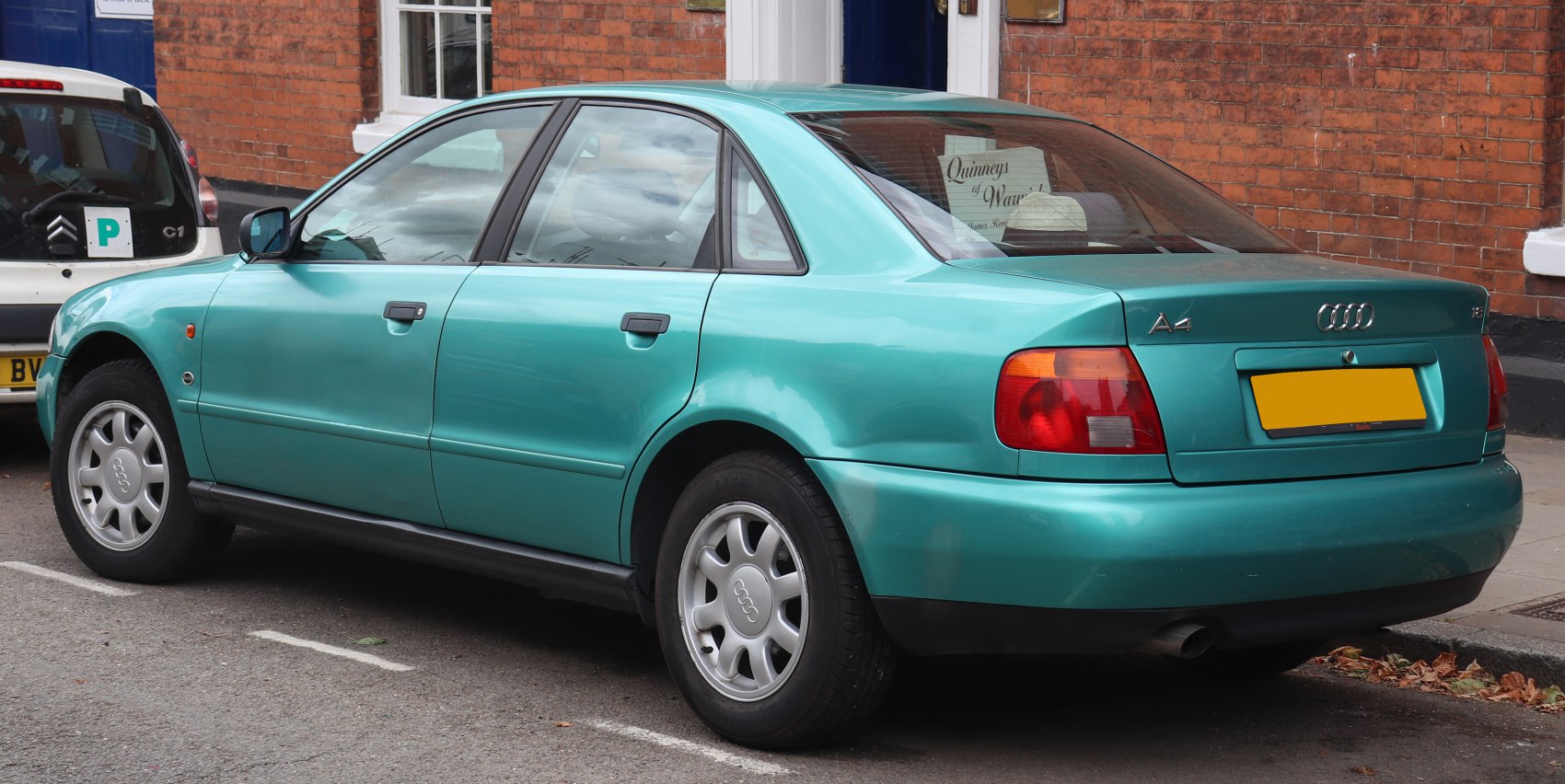 Rear side view of a teal classic sedan from the 1990s with distinctive tail lights and alloy wheels.