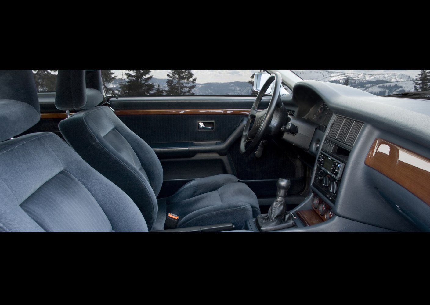 Classic car interior with plush seats, manual transmission, wood trim, and vintage dashboard.