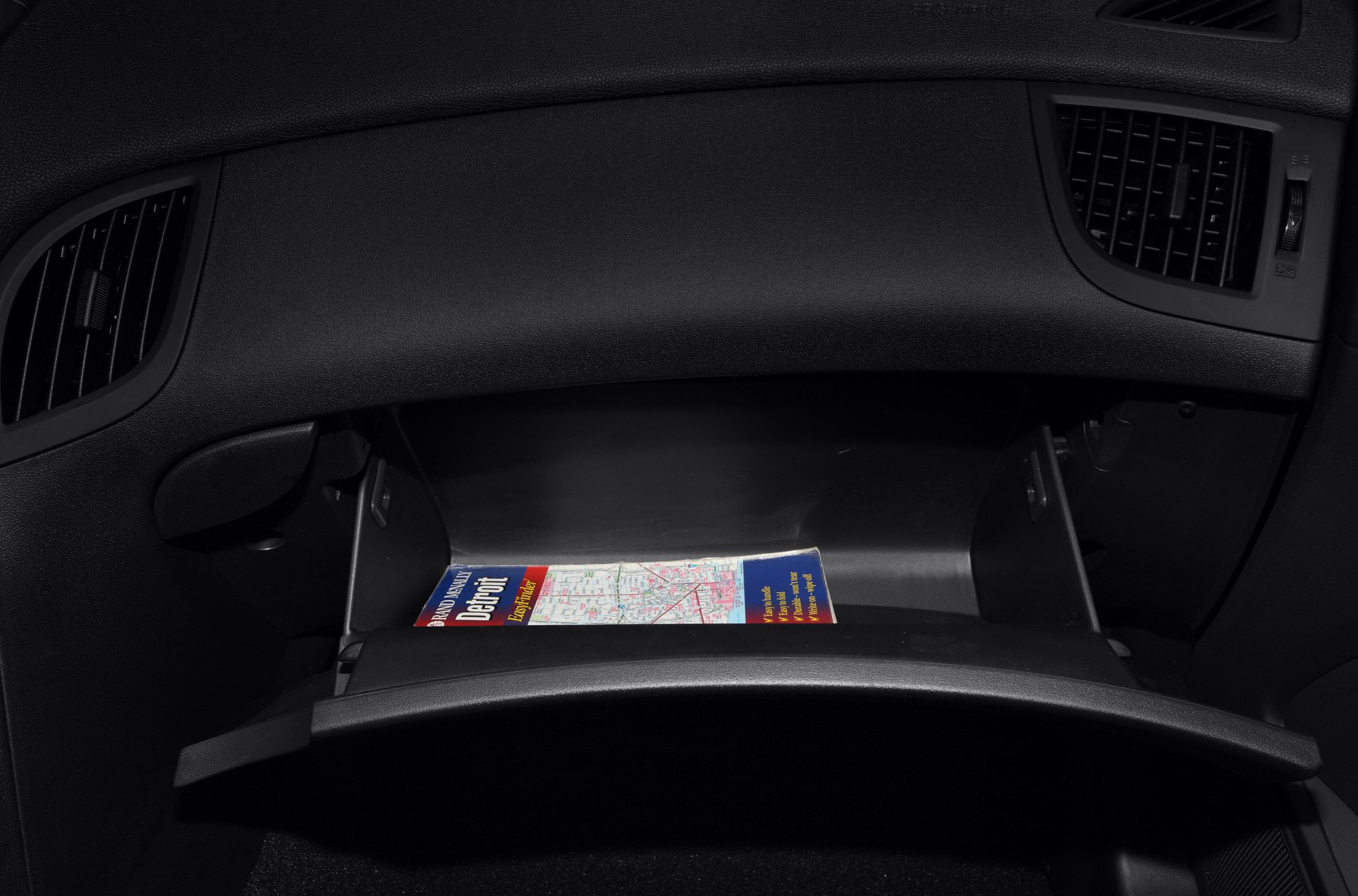 Open glove compartment with a folded map inside, flanked by air vents