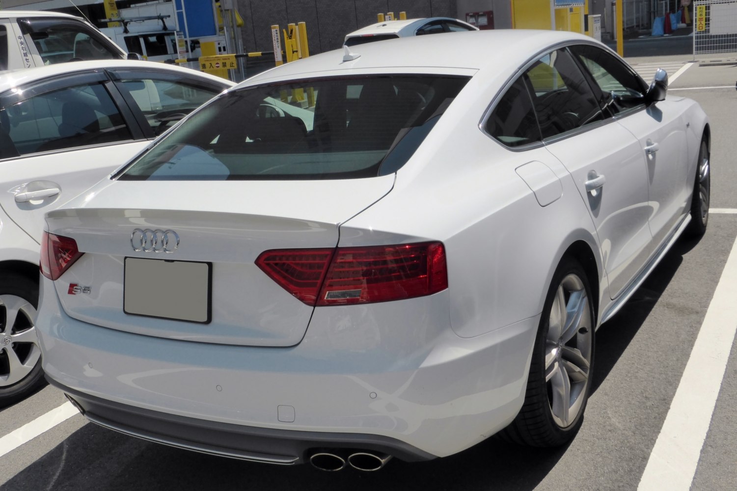 White sedan rear view with distinct taillights and quad exhaust pipes.