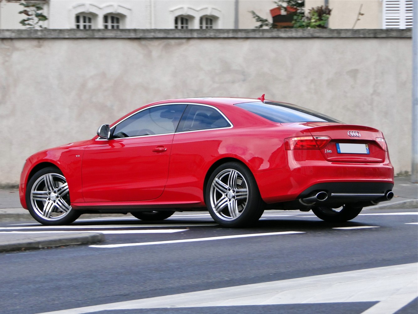 Red sporty coupe with dual exhaust and alloy wheels shown from rear side angle.