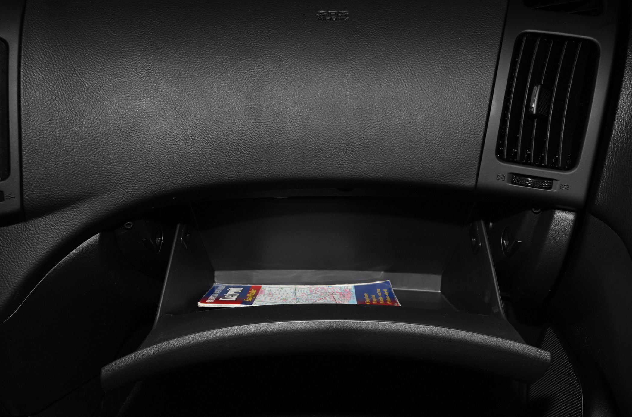Open glove compartment with map inside, dashboard air vent and SRS airbag detail
