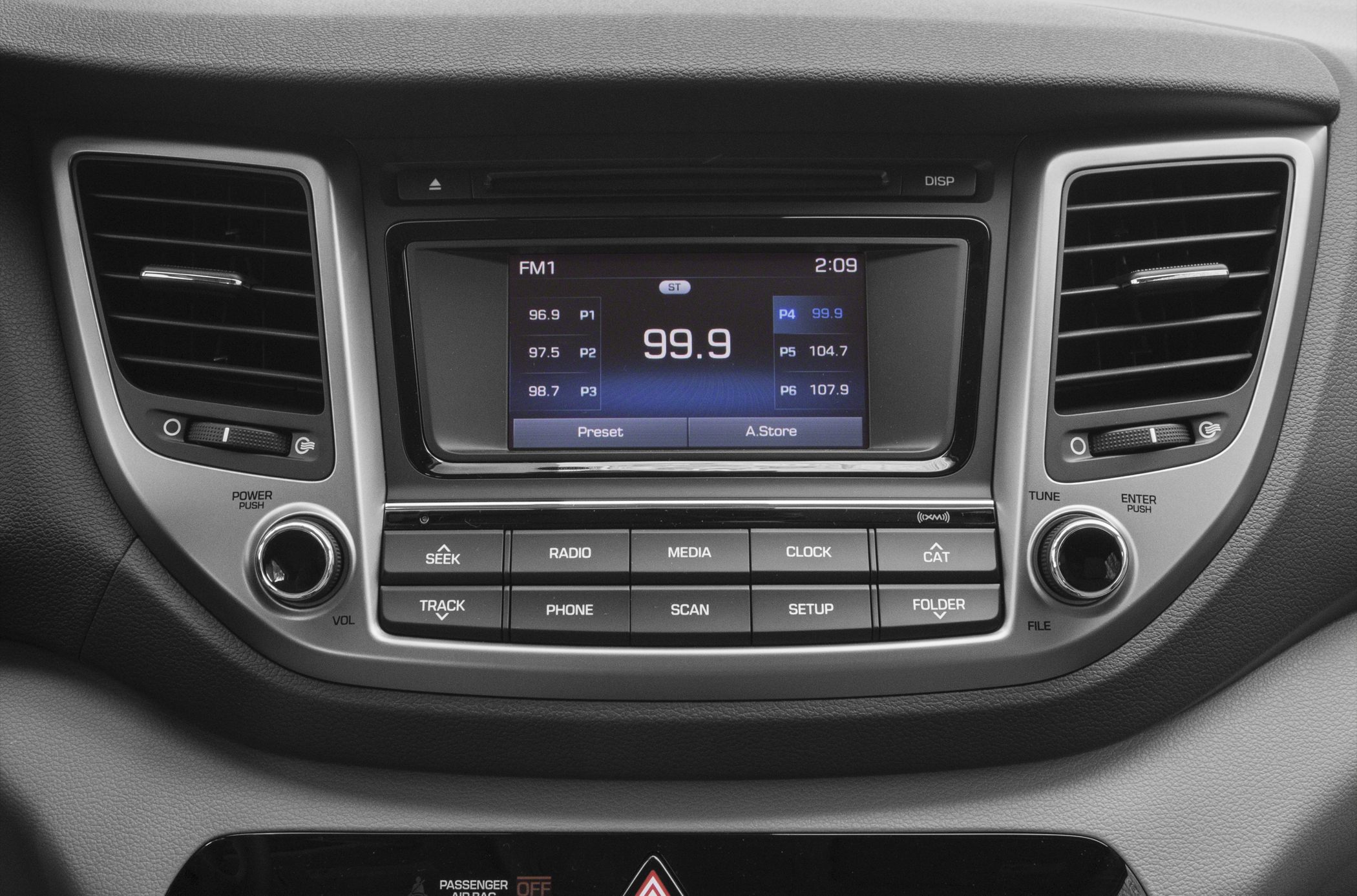 Close-up of car radio and dashboard air vents with media buttons and FM display.