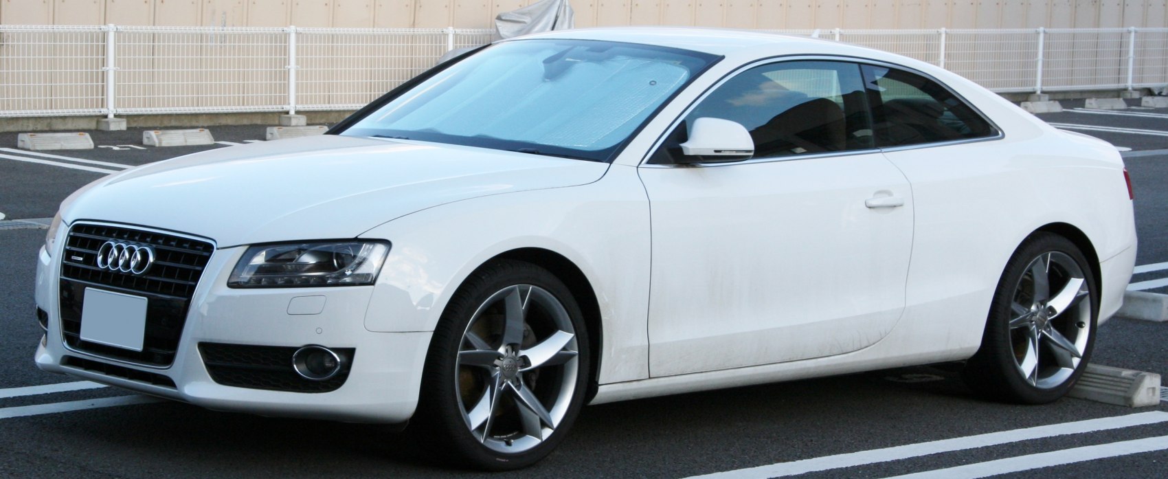 White coupe with sleek body and distinctive grille, alloy wheels visible
