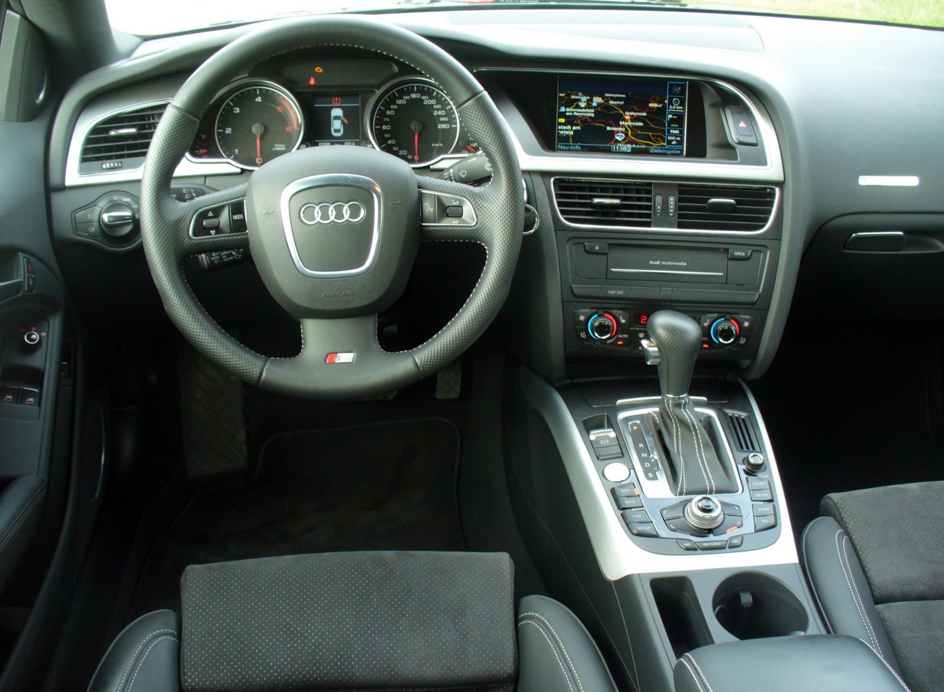 Audi interior with steering wheel, dashboard, multimedia screen, and center console.
