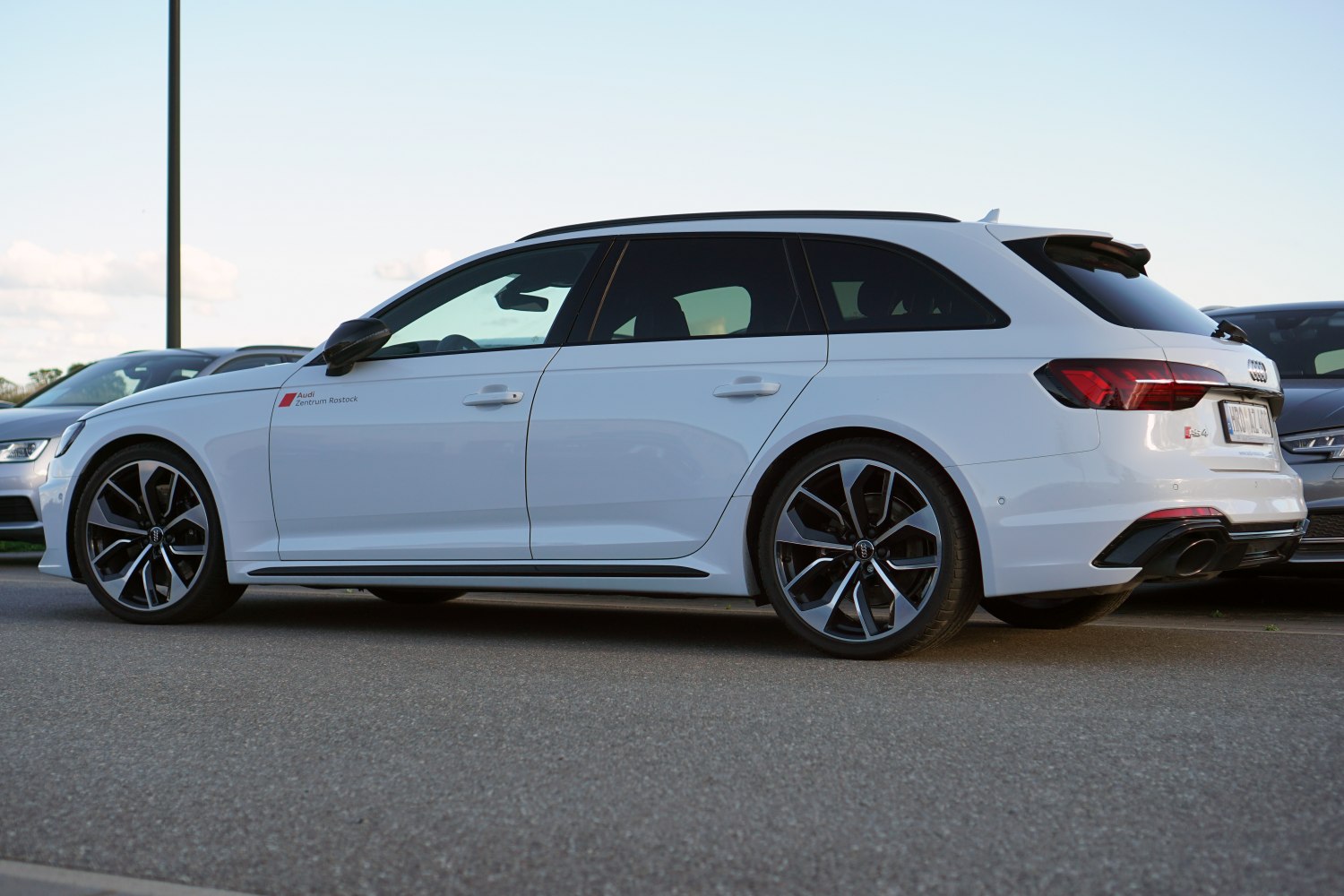 White sporty wagon with black multi-spoke wheels and dual exhaust
