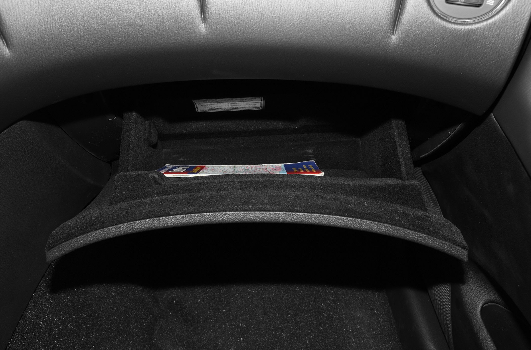 Black glove box storage compartment with a map inside.