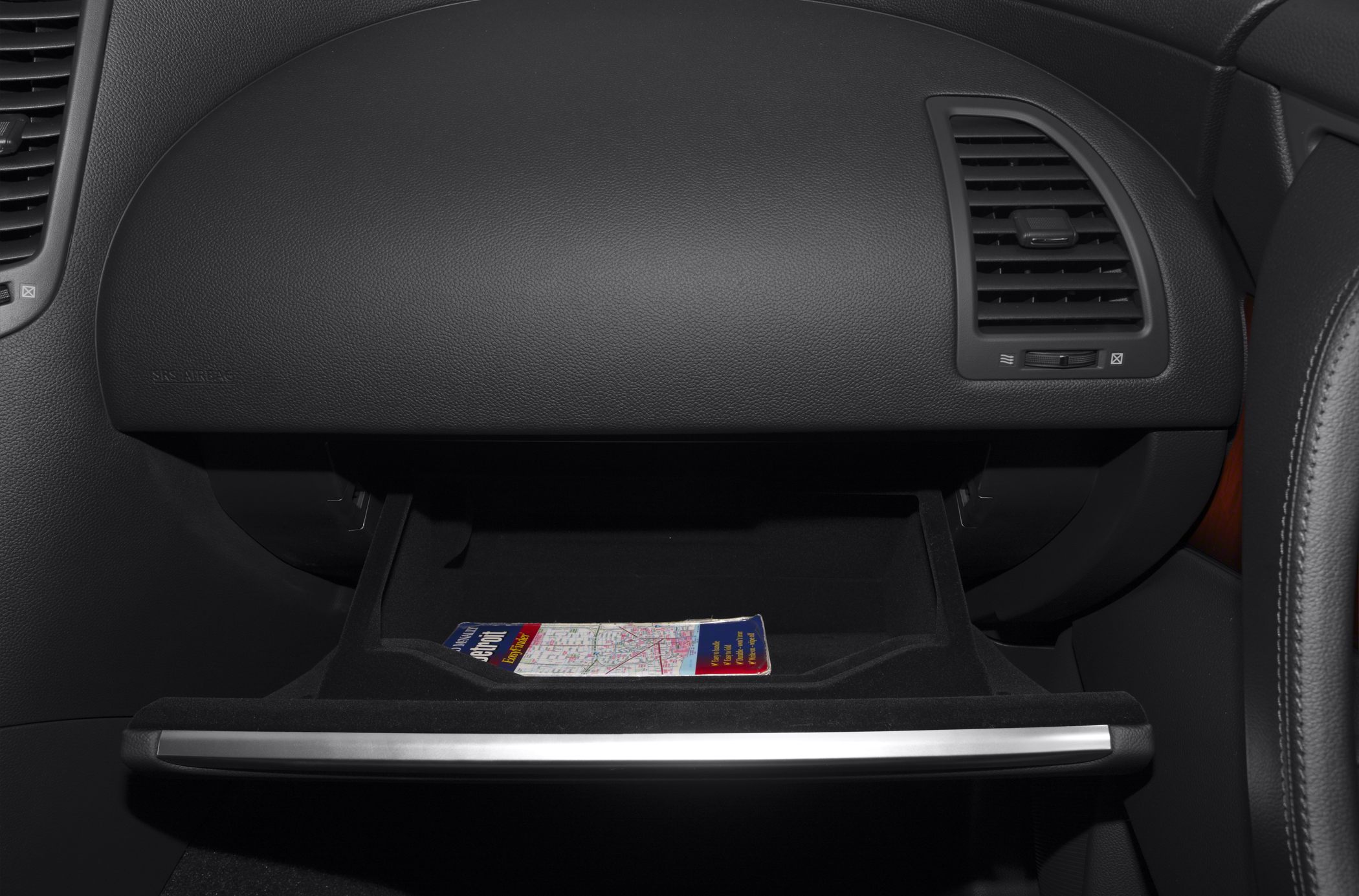 Open glove box with map and dashboard air vent in black leather interior