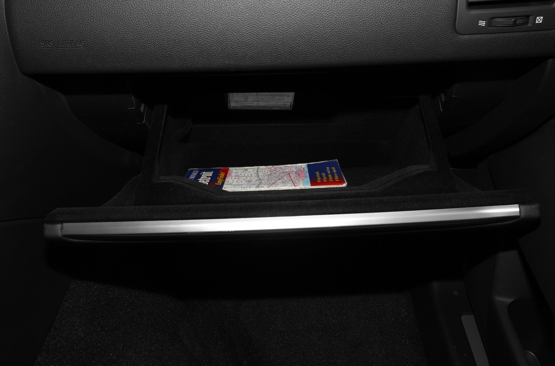 Close-up of an open glove compartment with storage space and map inside.