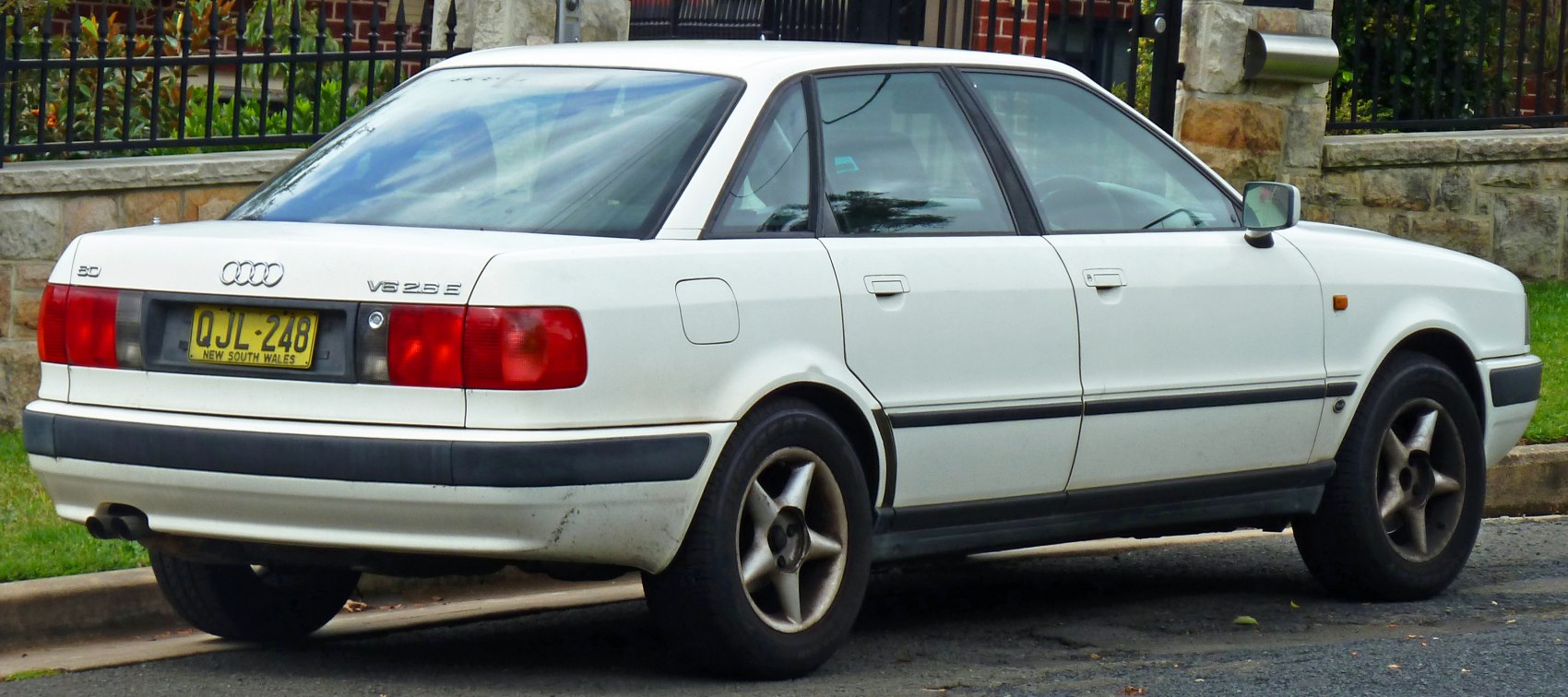 Rear and side view of white classic sedan with alloy wheels and visible taillights.