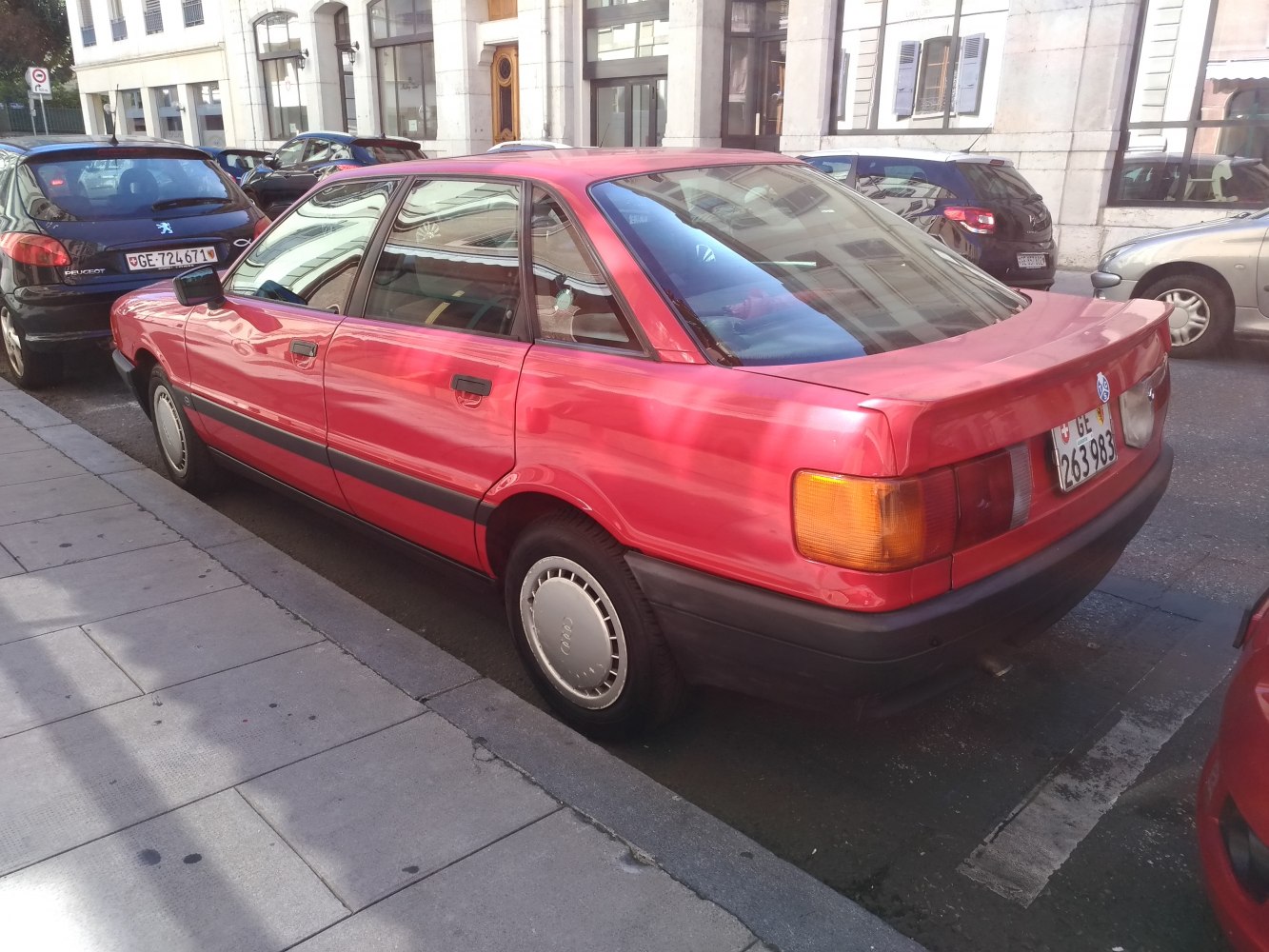 Red 1980s sedan rear side view with boxy shape and distinct tail lights
