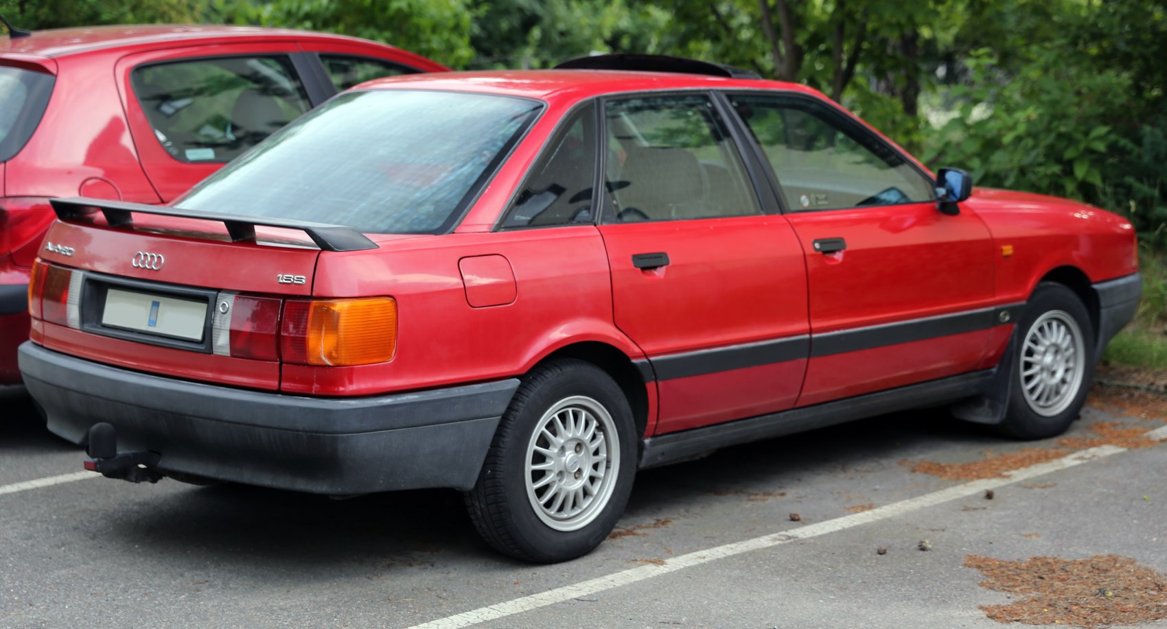 Rear side view of red sedan with rear spoiler and alloy wheels