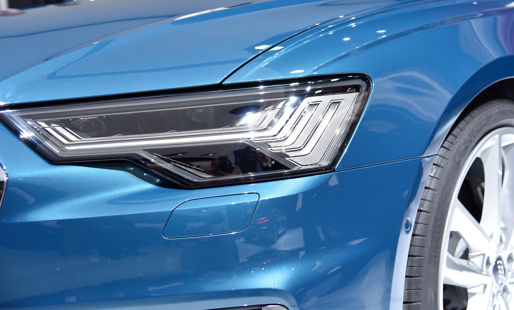 LED headlight with intricate design and front wheel of blue sedan