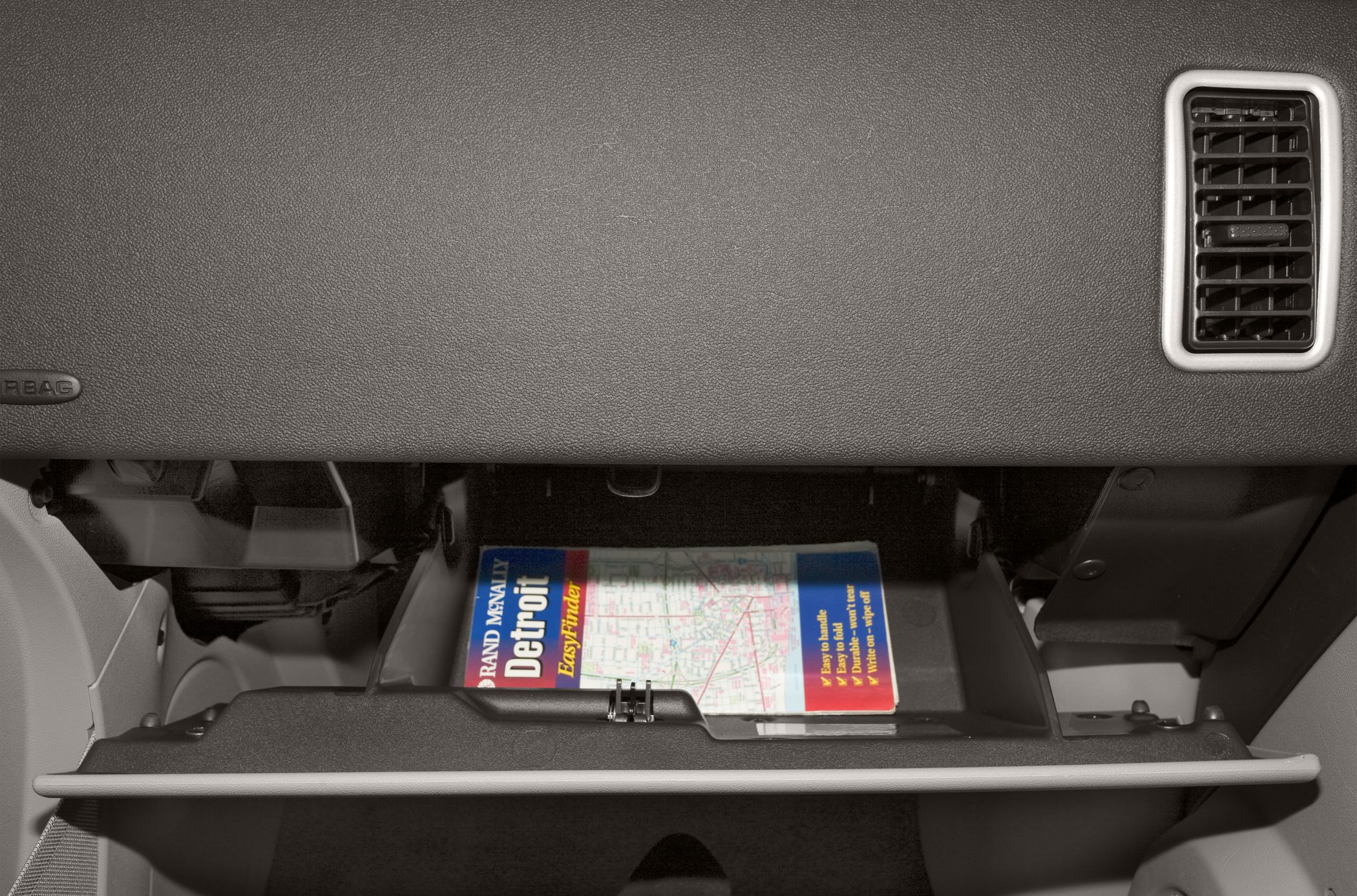 Open glove compartment with a map inside and dashboard air vent.