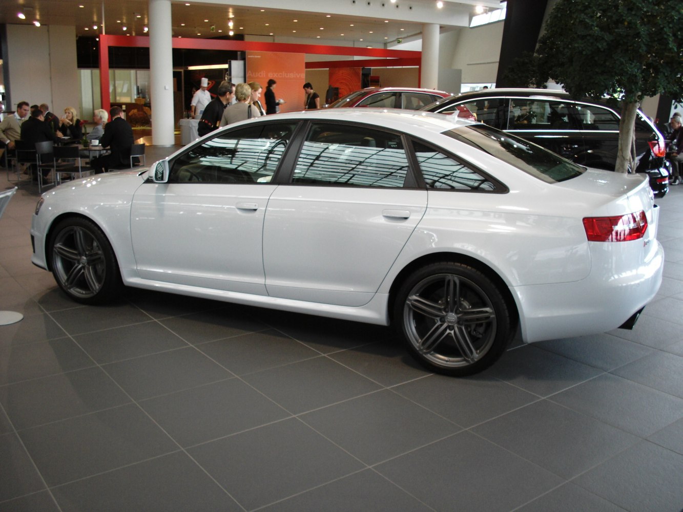 White sedan side view with distinctive alloy wheels in a showroom.