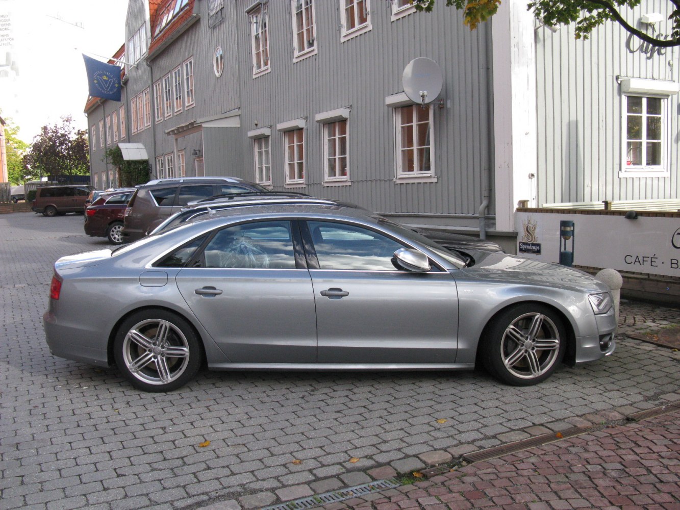 Silver luxury sedan side profile on cobblestone street.