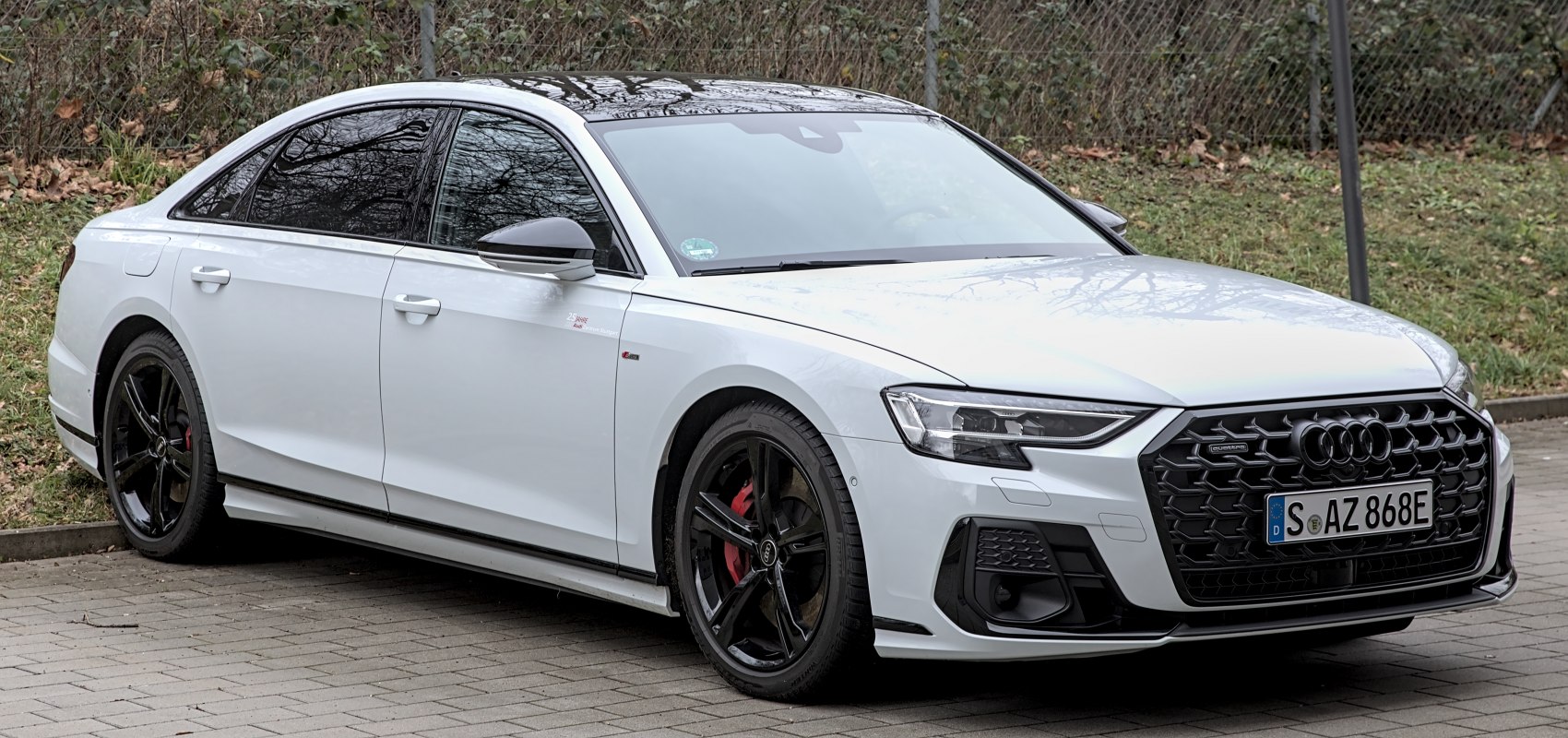 White luxury sedan with black wheels, black grille, and red brake calipers.