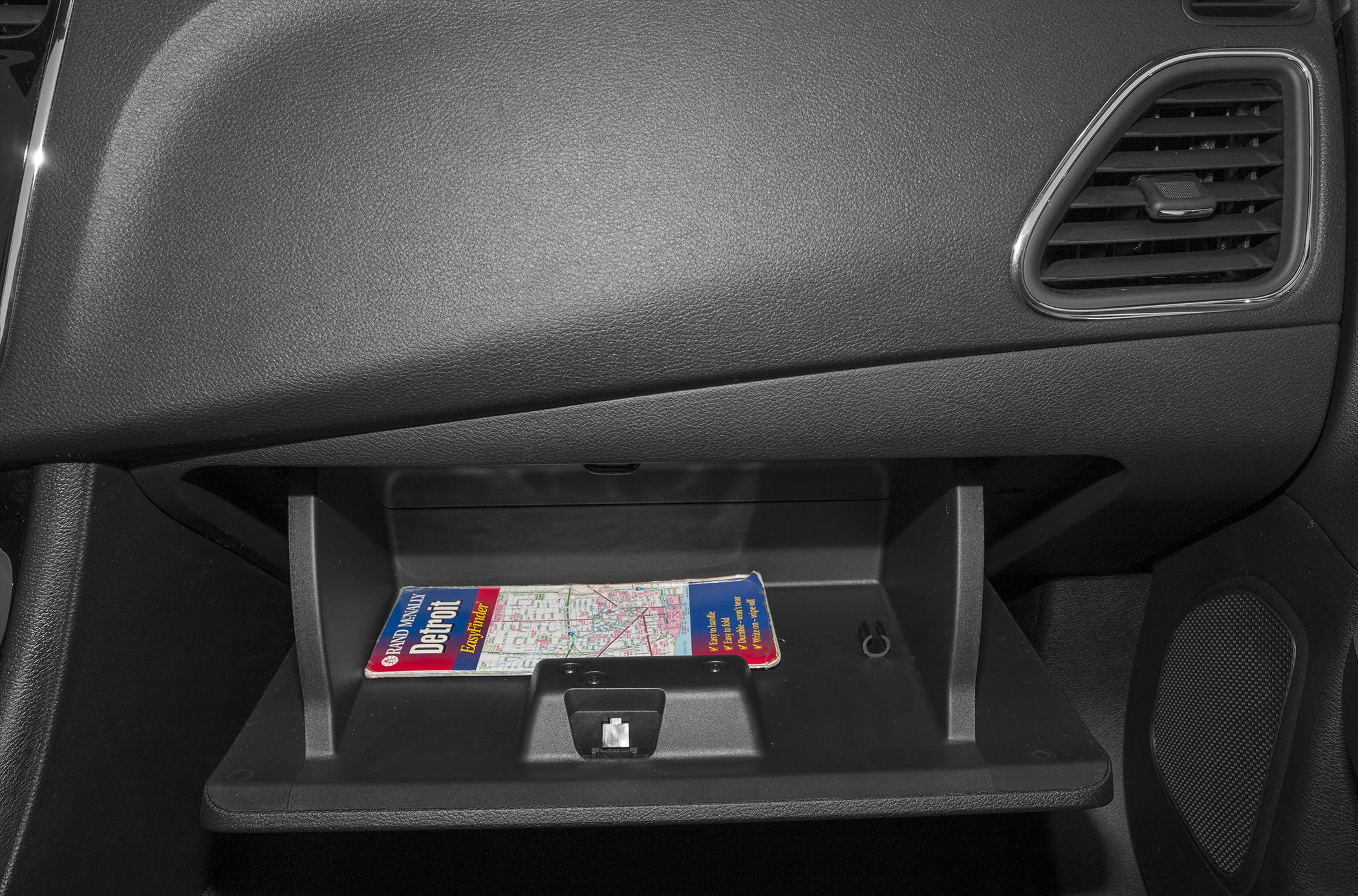 Open glove box with a map and dashboard air vent.