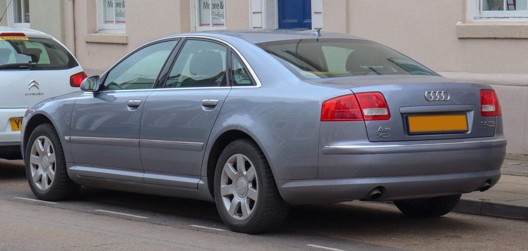 Rear and side view of a silver luxury sedan with dual exhausts and large red tail lights.