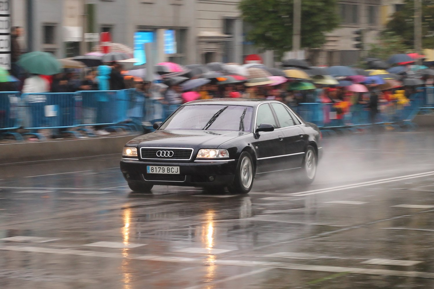 Luxurious black sedan driving fast on wet road with water spray and reflections