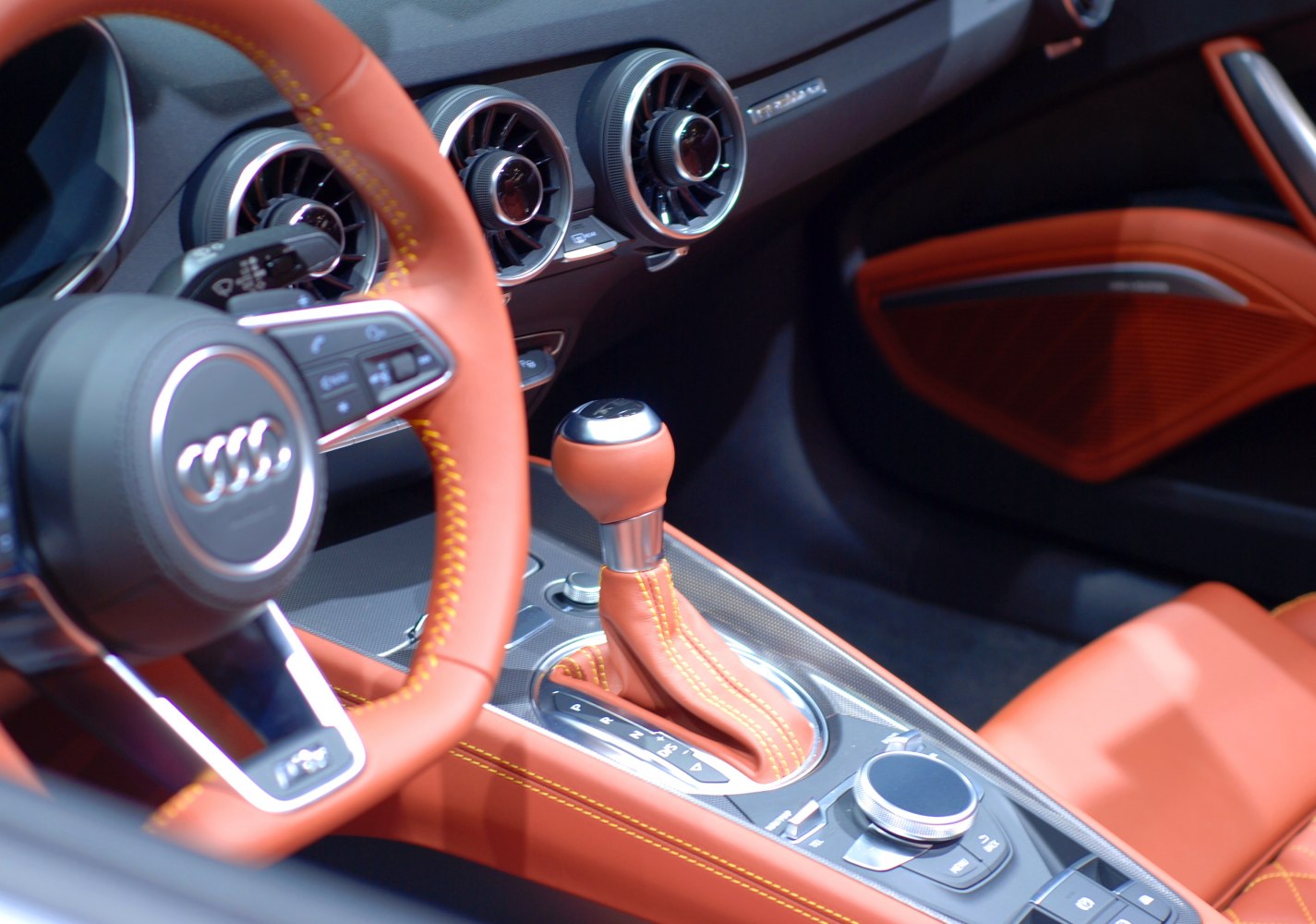 Interior close-up of gear shifter and dashboard air vents with orange leather trim