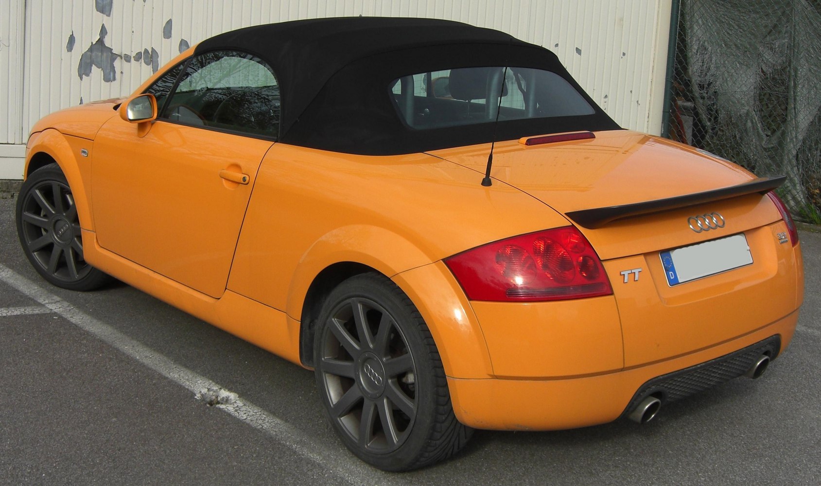 Orange convertible with black soft top and dual exhaust rear view