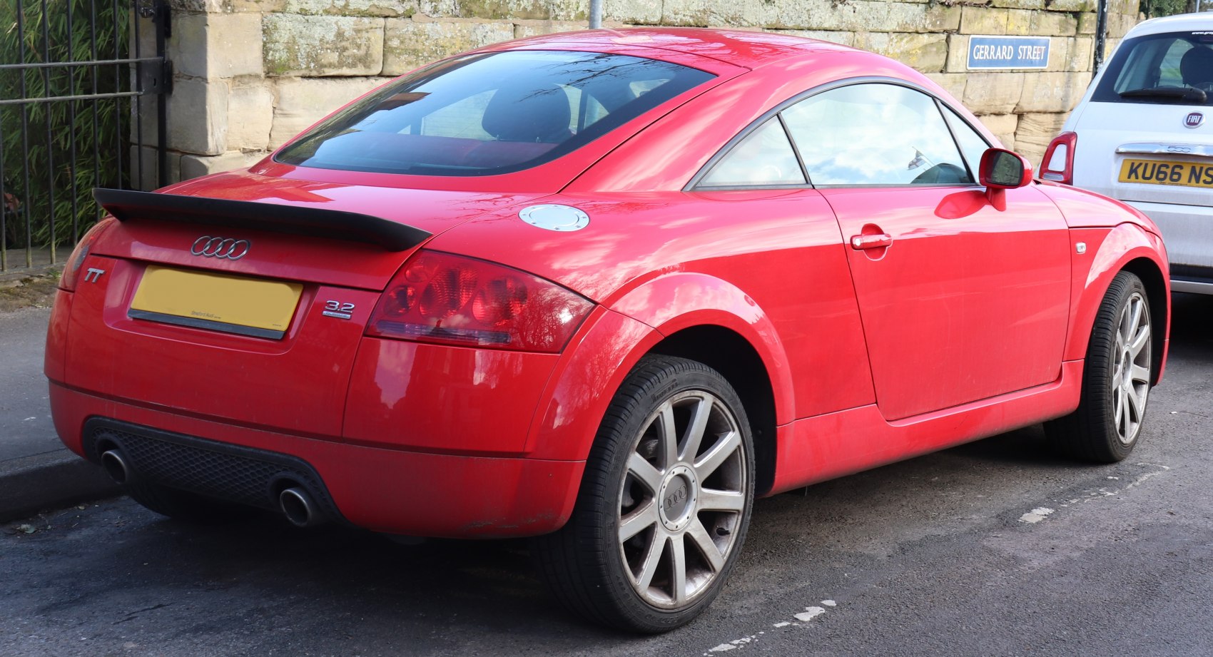 Rear side view of red coupe with spoiler and alloy wheels.