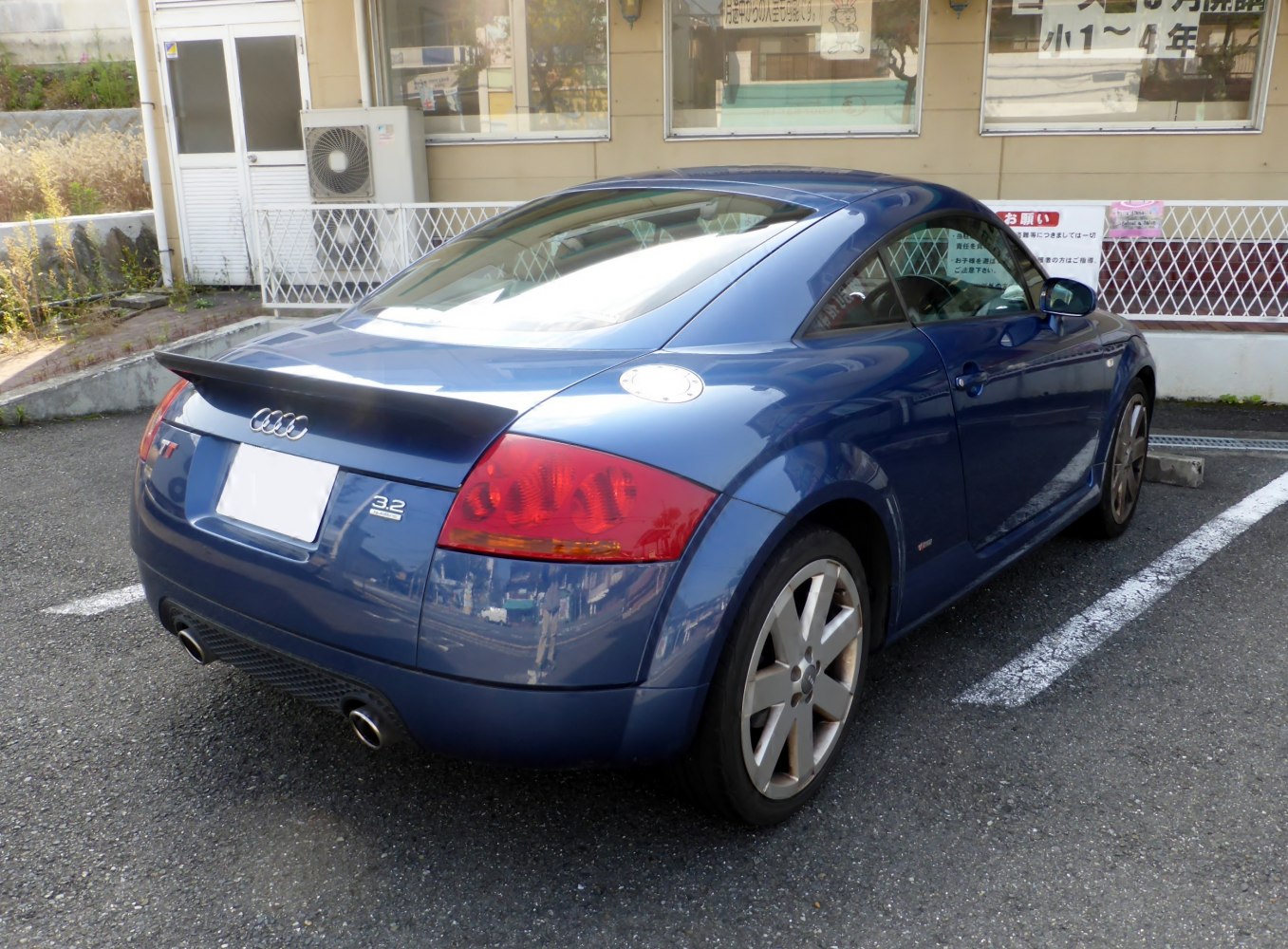 Rear side view of blue sports coupe with spoiler and dual exhaust.